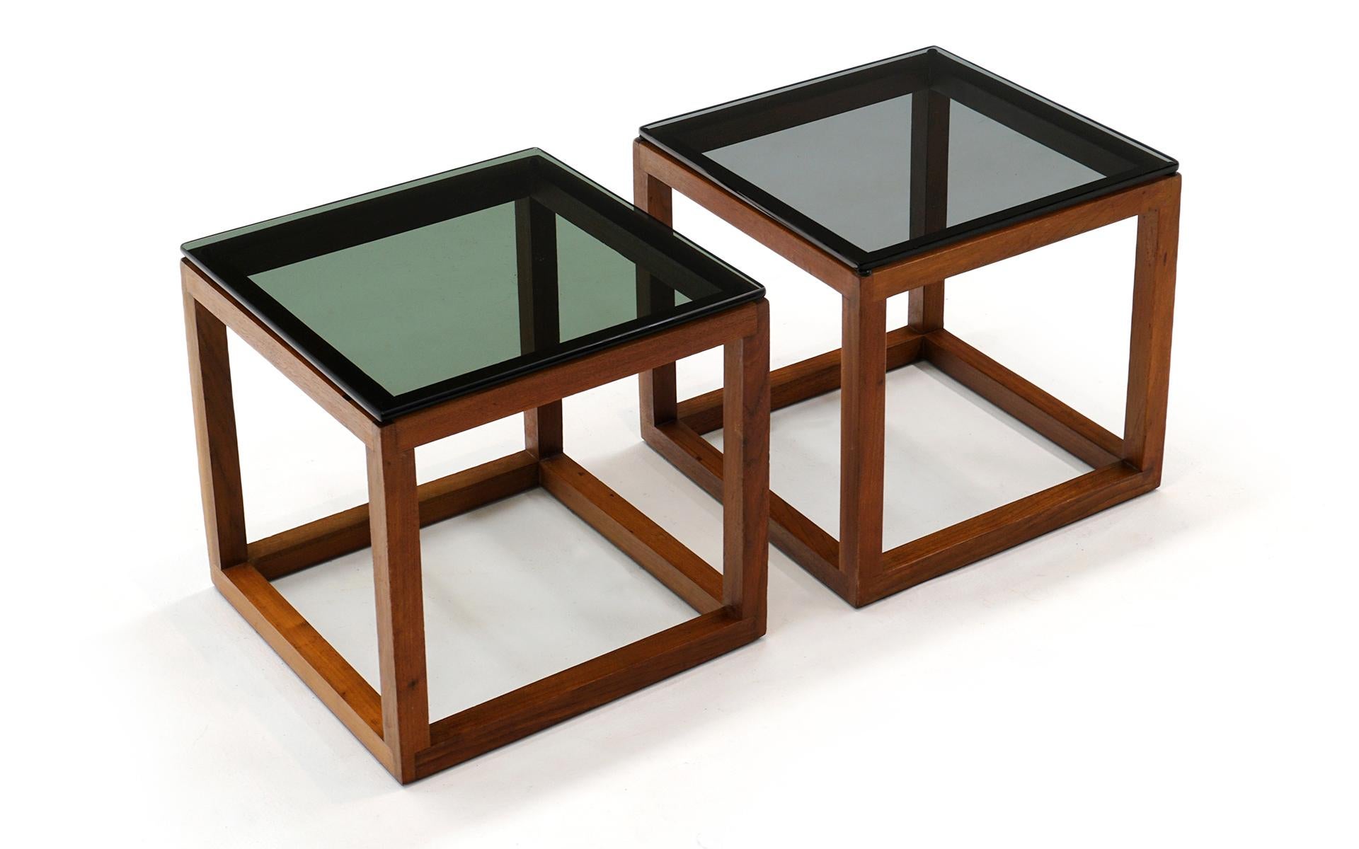 Pair of teak and grey glass end / side tables. The frames are solid teak with dovetailed joints. The glass is 3/8ths inches thick with rounded edges. Under a lot of light it is evident that one glass top is slightly darker than the other. This is