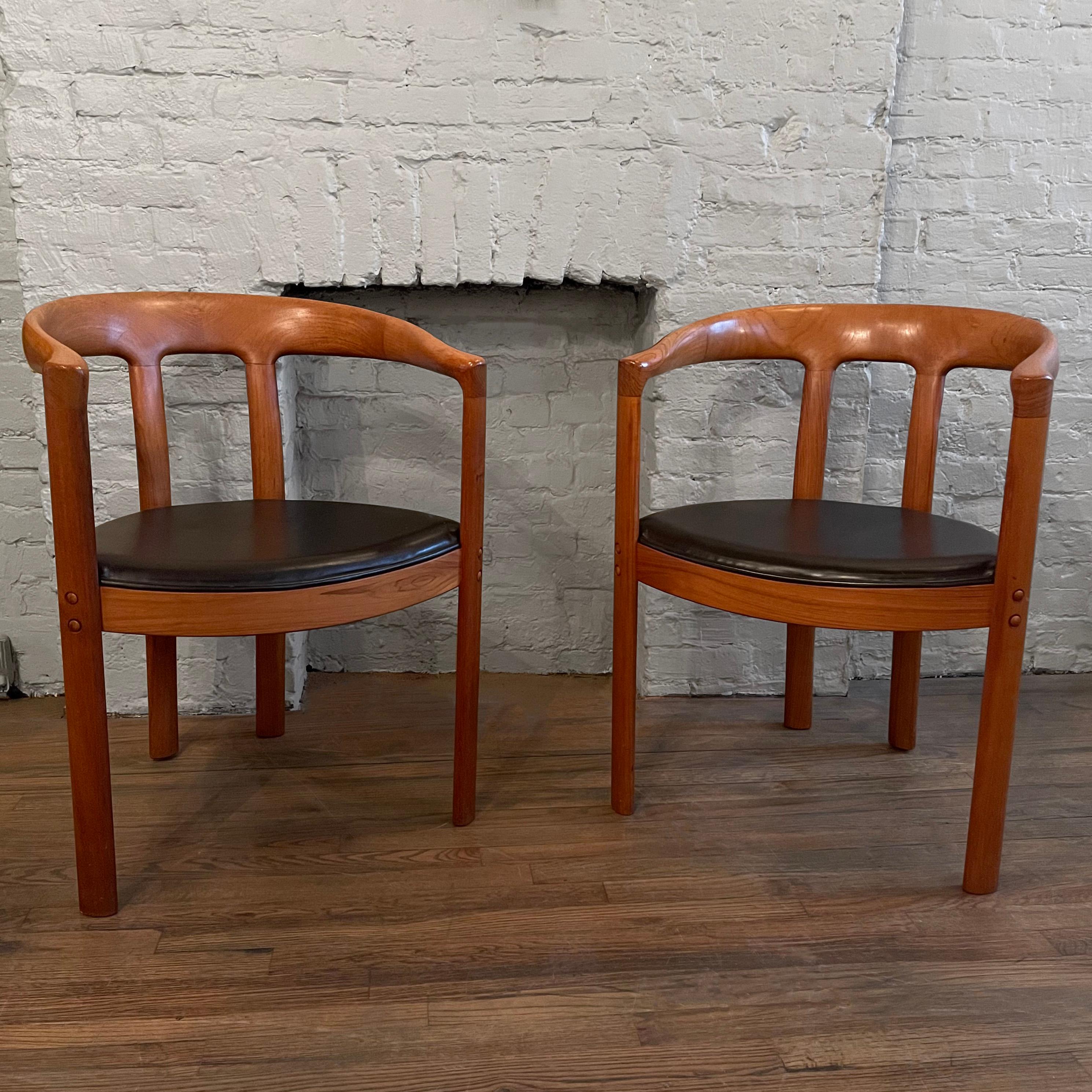 Pair of Danish modern, teak, barrel chairs with thick rounded frames and black vinyl seats. Their arm height measures 27.75 inches.