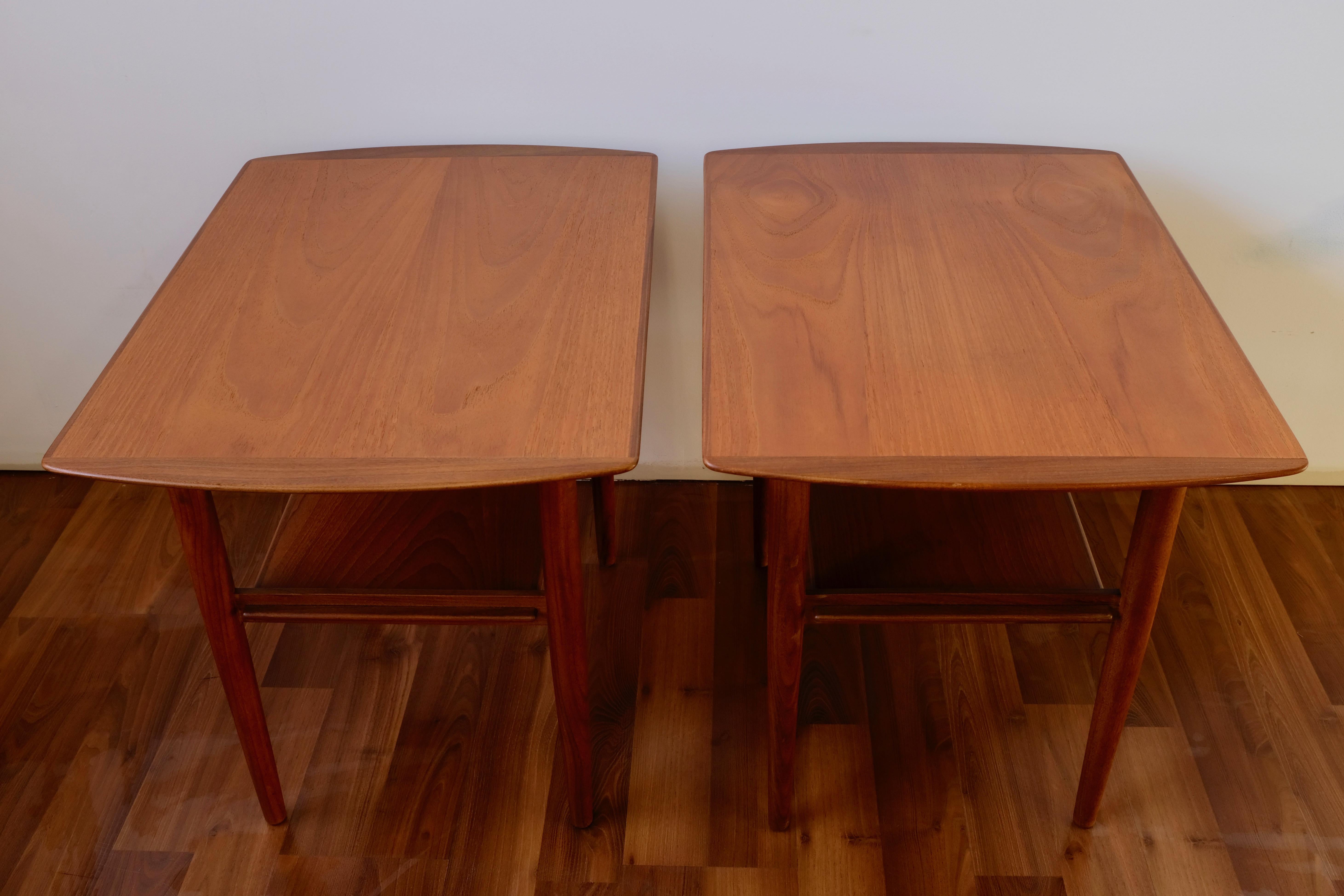 Two matching end tables each with a single shelf below the top. The frames are constructed of solid teak while the tops and shelves are constructed of a solid wood core with teak veneer and solid teak edging. 

The tables have been refinished and