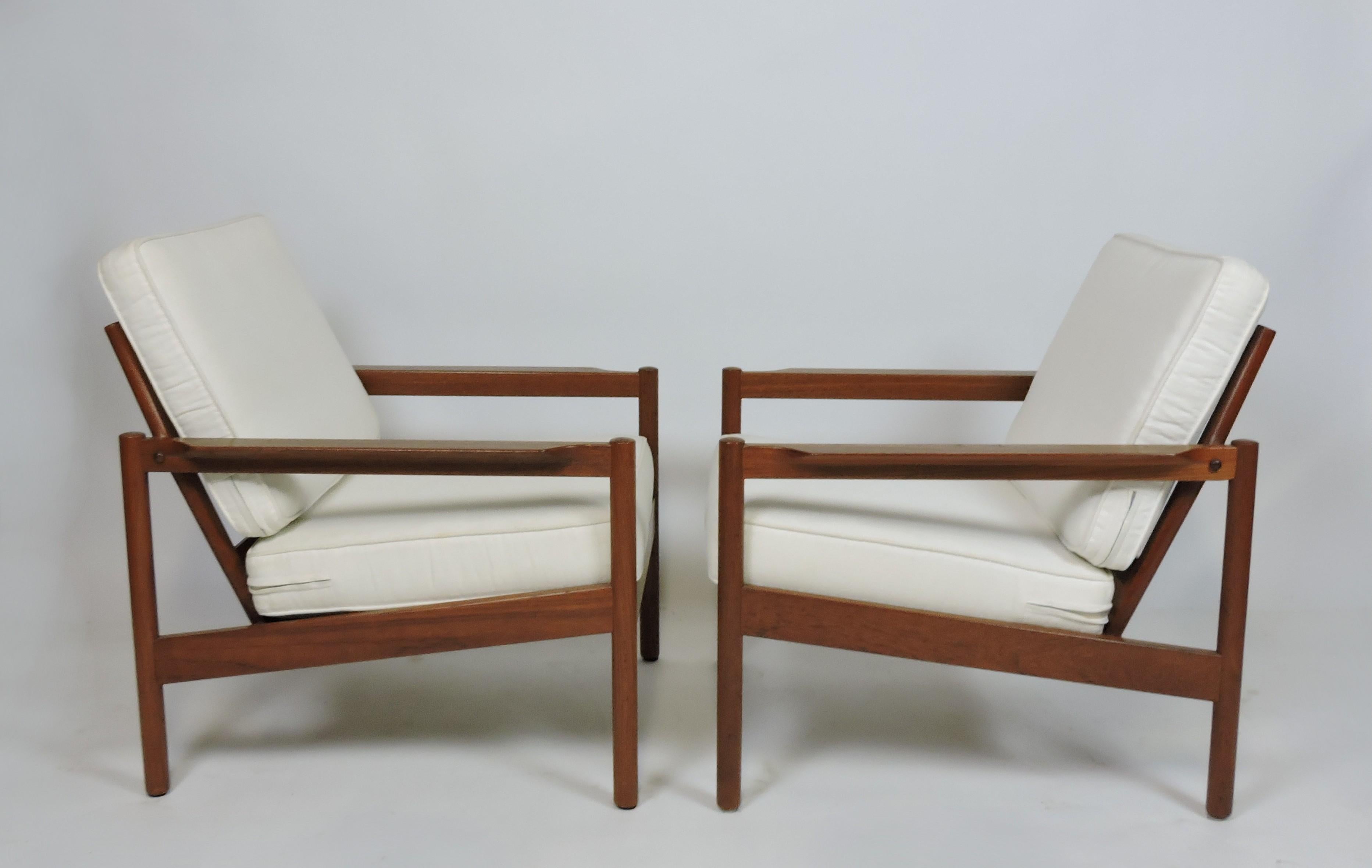 Handsome pair of open arm lounge chairs, model KK161, designed by Kai Kristiansen and manufactured in Denmark by high-quality furniture maker, Magnus Olesen. These very comfortable chairs are made of solid teak with two loose cushions that are