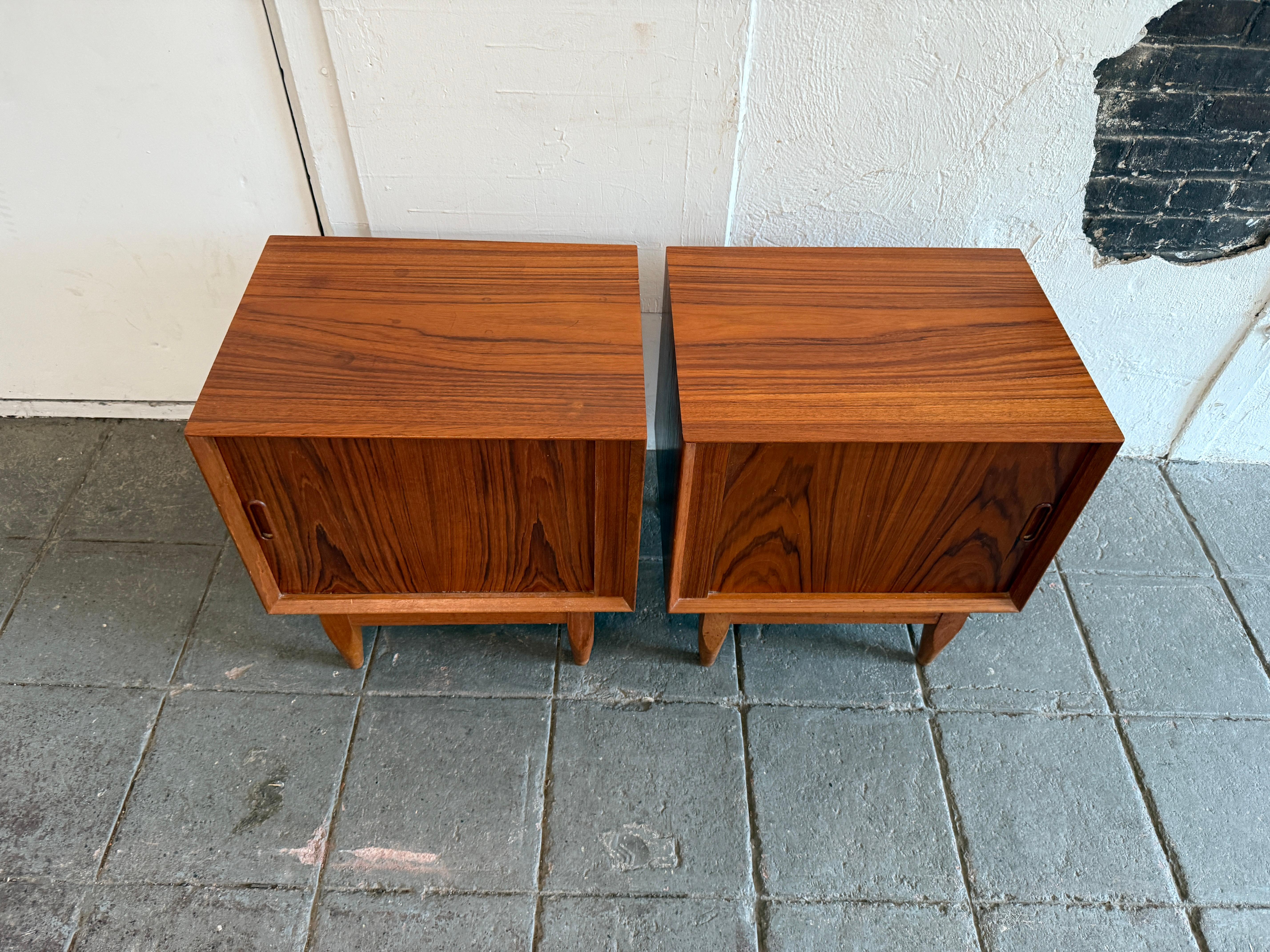 Paire de tables de nuit modernes danoises en teck à porte tambour. Superbe ensemble de tables de nuit danoises avec portes coulissantes, un tiroir et une étagère réglable derrière les portes. Bon état général. Ils reposent sur (4) pieds effilés.