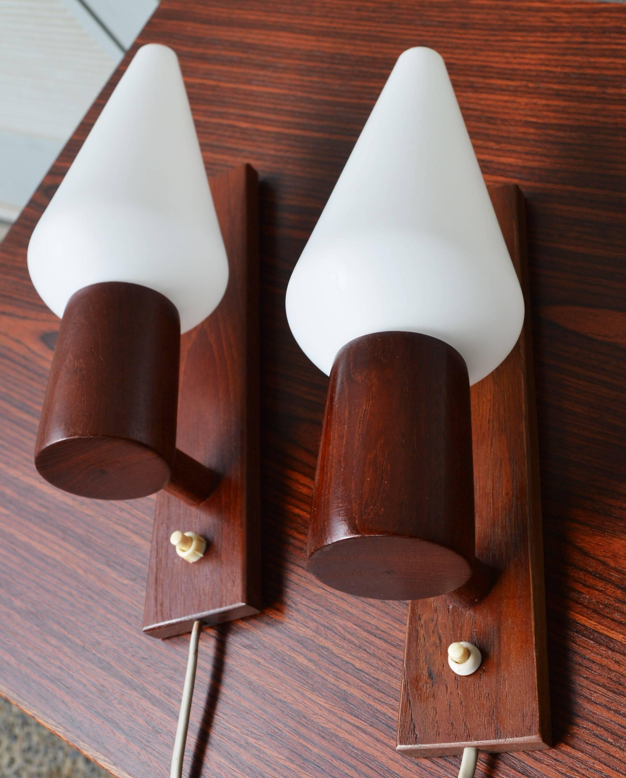 This stellar pair of rare Danish modern teak wall sconces are cleverly designed with the switch on the sconce and a long cord to plug into the wall - freeing you from the need to get them professionally hard wired into the wall by an electrician,