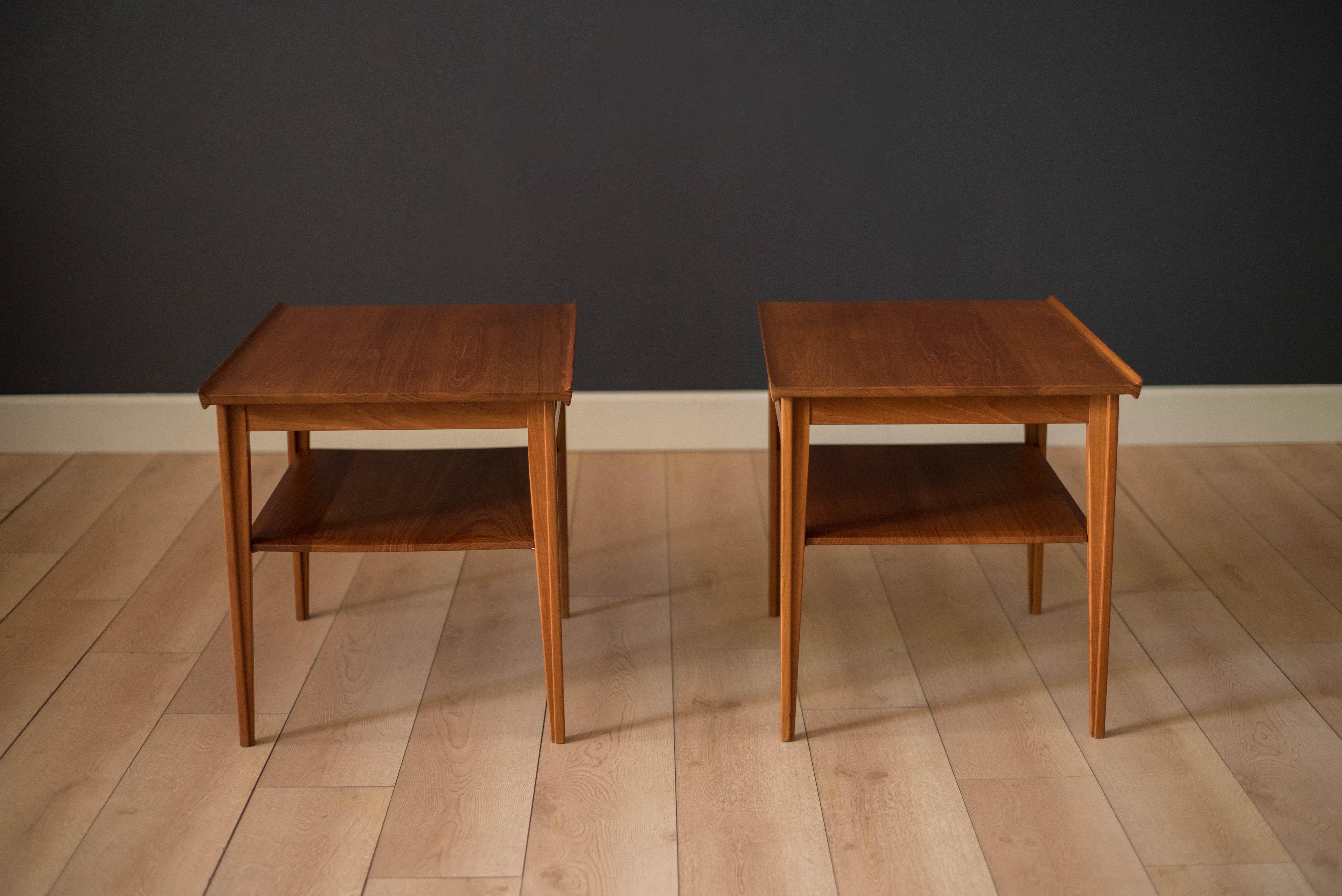 Mid-Century Modern pair of side tables designed by Finn Juhl for France & Søn. Produced after the Japan series, this set is made of solid teak construction designed with sculpted raised edges and striking tapered legs. Lower beveled shelf is