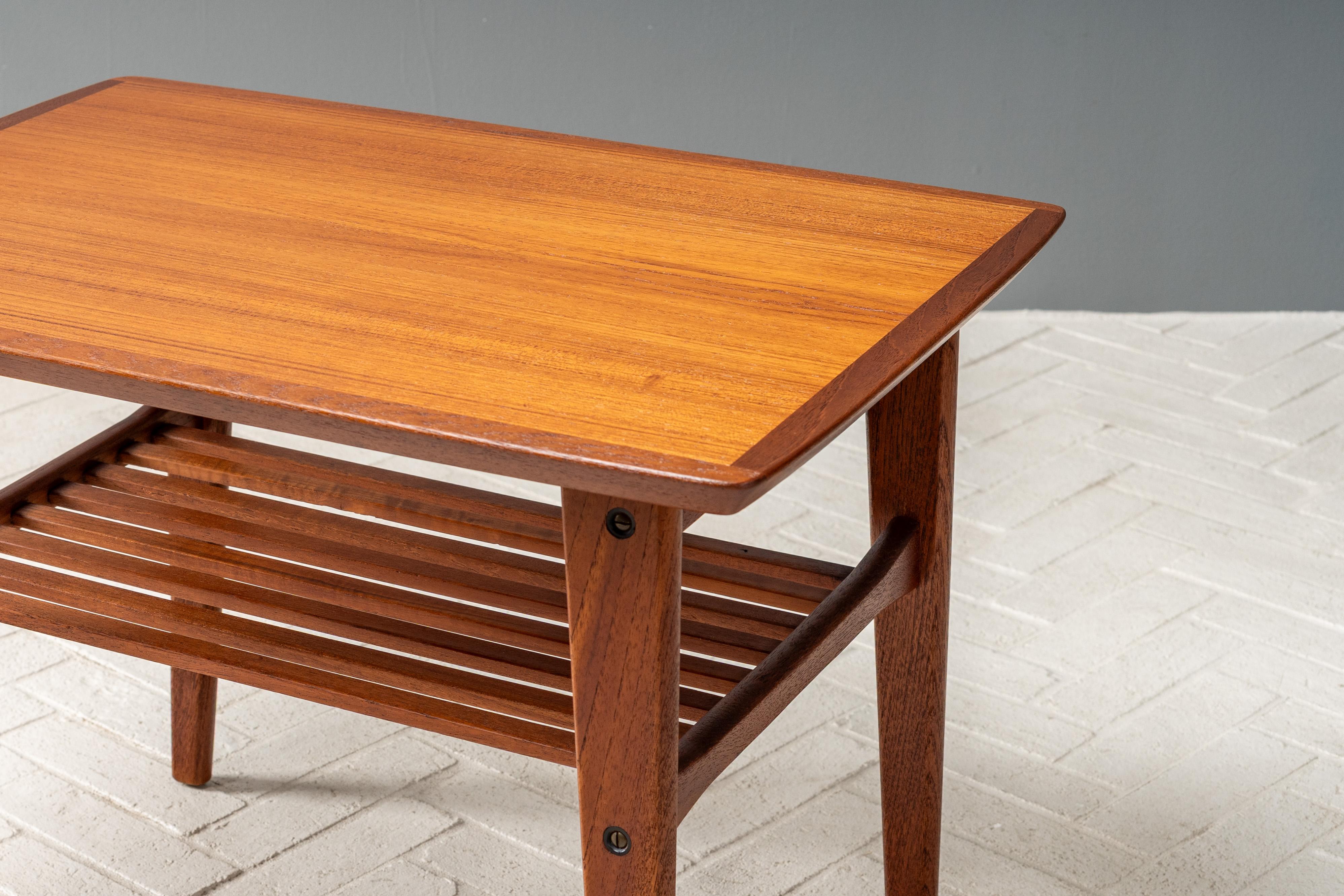 Danimarca, anni '60 circa. Un'elegante coppia di tavolini di EW Bach per Toften. Ciascuna è realizzata in teak con un piano rettangolare leggermente svasato sostenuto da gambe triangolari affusolate. L'attraente scaffale a doghe è il nascondiglio