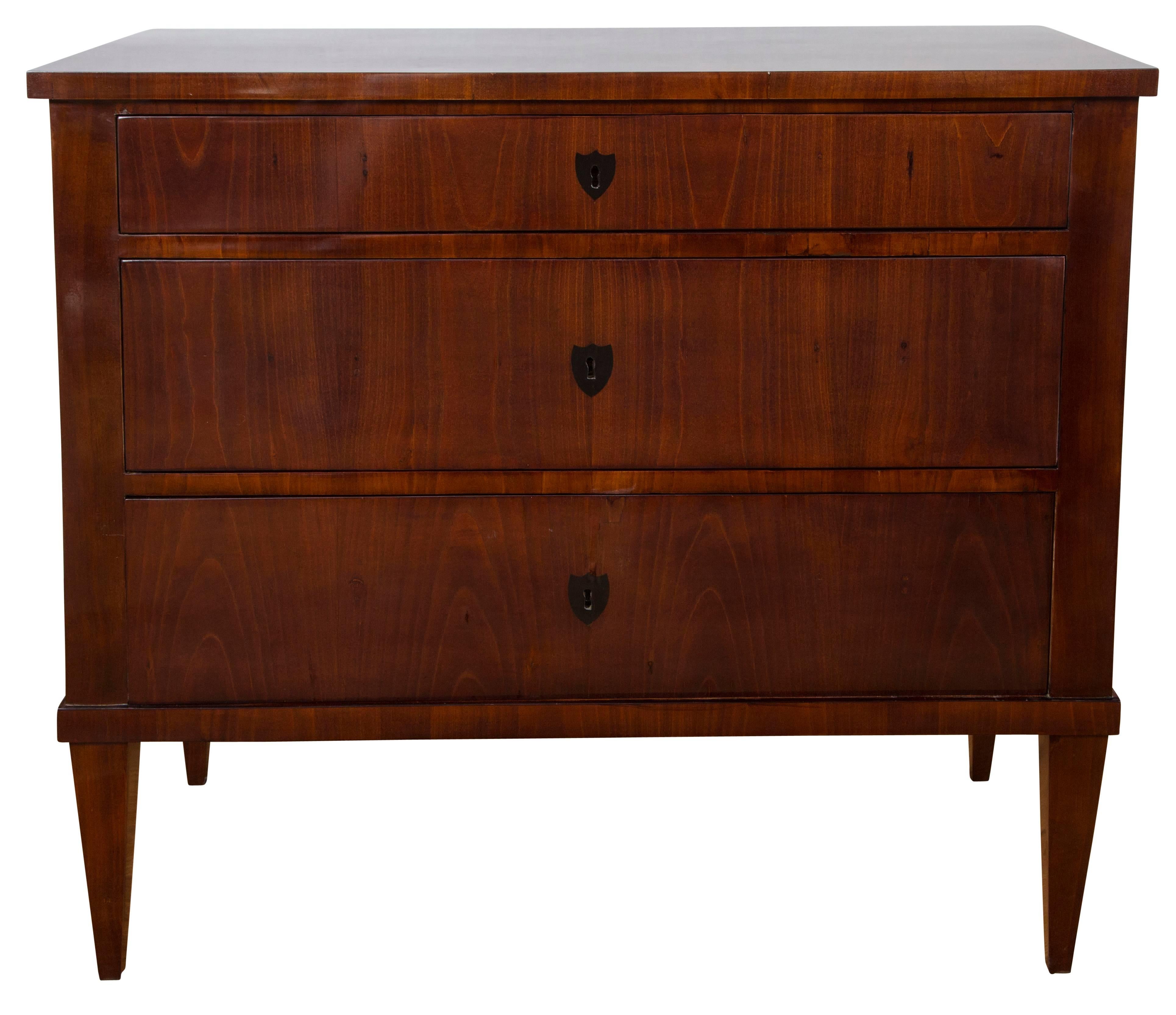 Pair of sleek Biedermeier chests comprised of three drawers finishing on straight and tapered legs in a dark cherrywood, adorned with stained inlaid shield-shaped escutcheons, a working key for each drawer is provided
Origin: Germany
Dating: