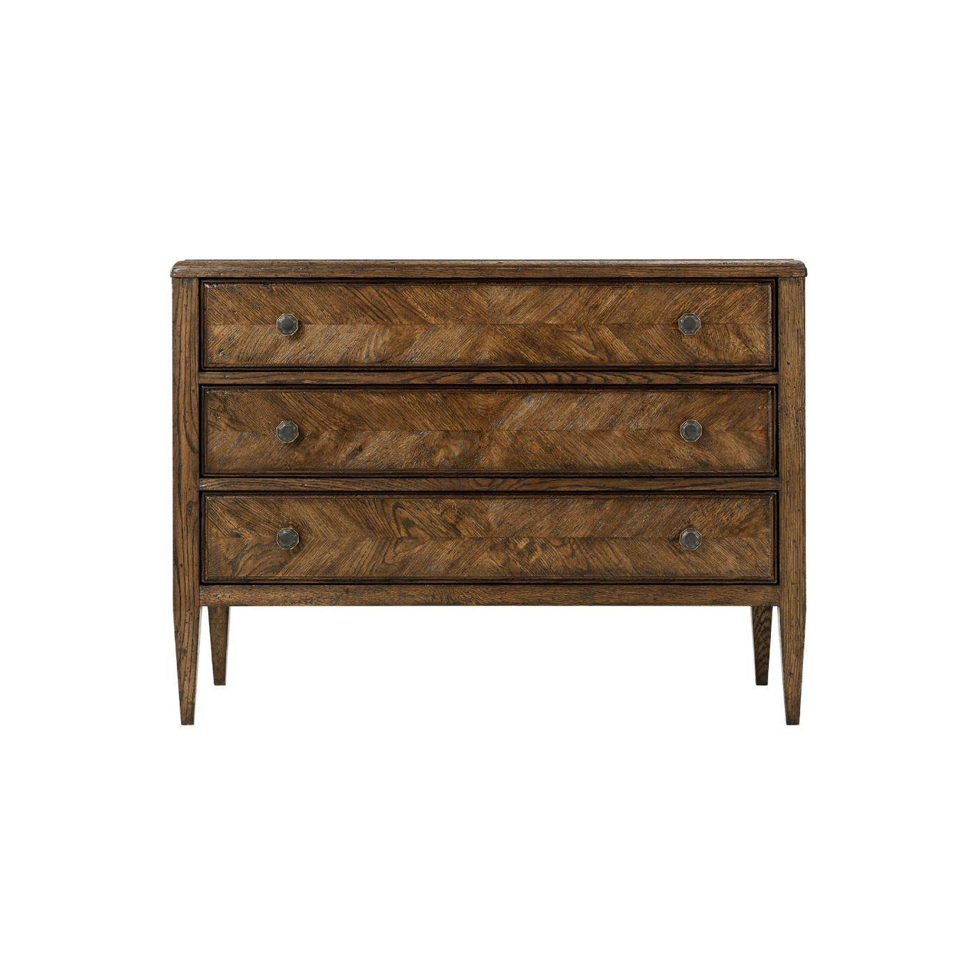A dark oak parquetry chest of drawers in Dusk finish. It has mirrored herringbone oak parquetry drawers, classically tapered legs, and six Verde Bronze finish handles. 
Shown in Dusk finish.
Dimensions: 38