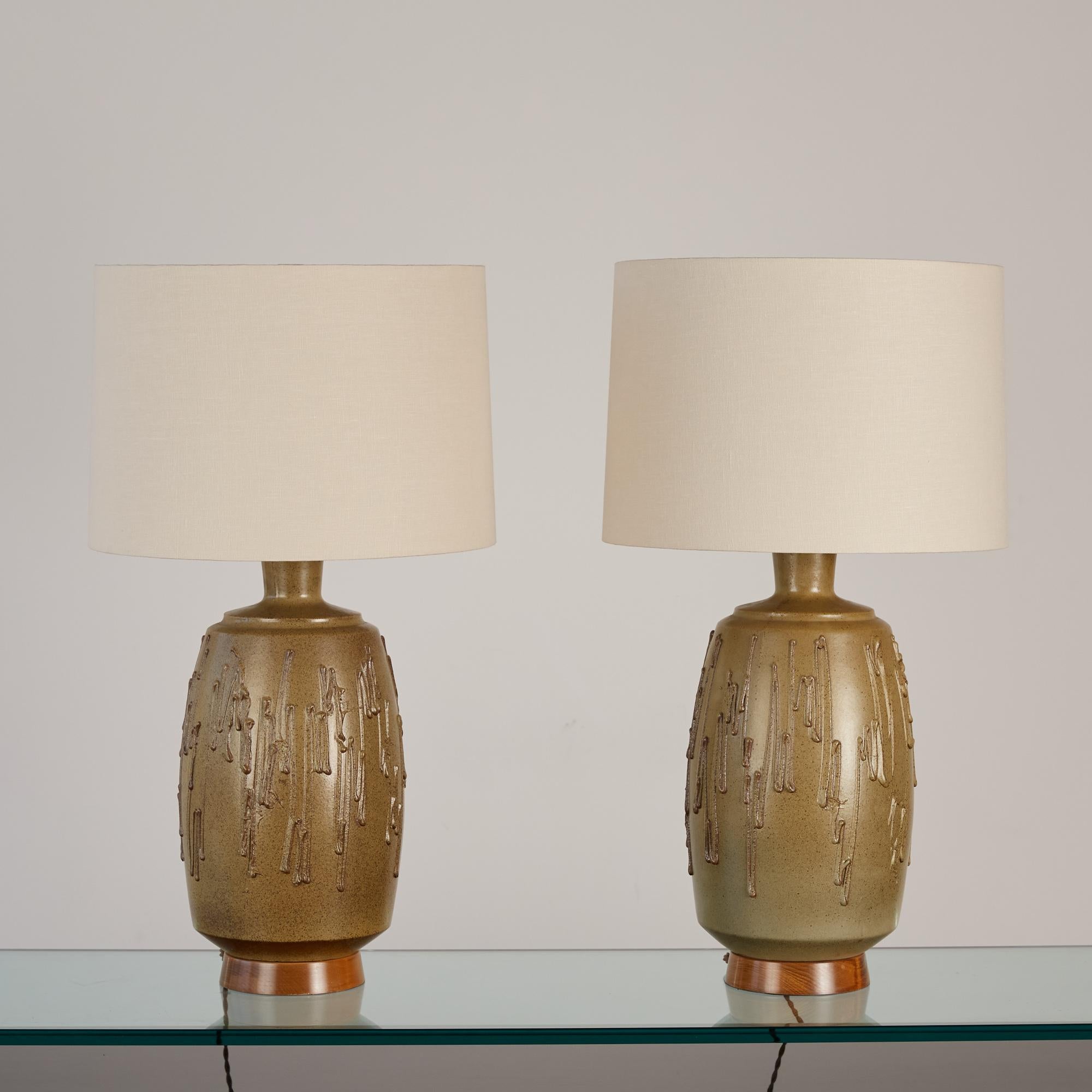 Pair of David Cressey stoneware lamps, USA, c.1960s. The wheel thrown stoneware lamps feature a speckled olive colored glaze with applied textured drip details. The ceramic form sits atop a turned oiled walnut base. The newly rewired lamps feature