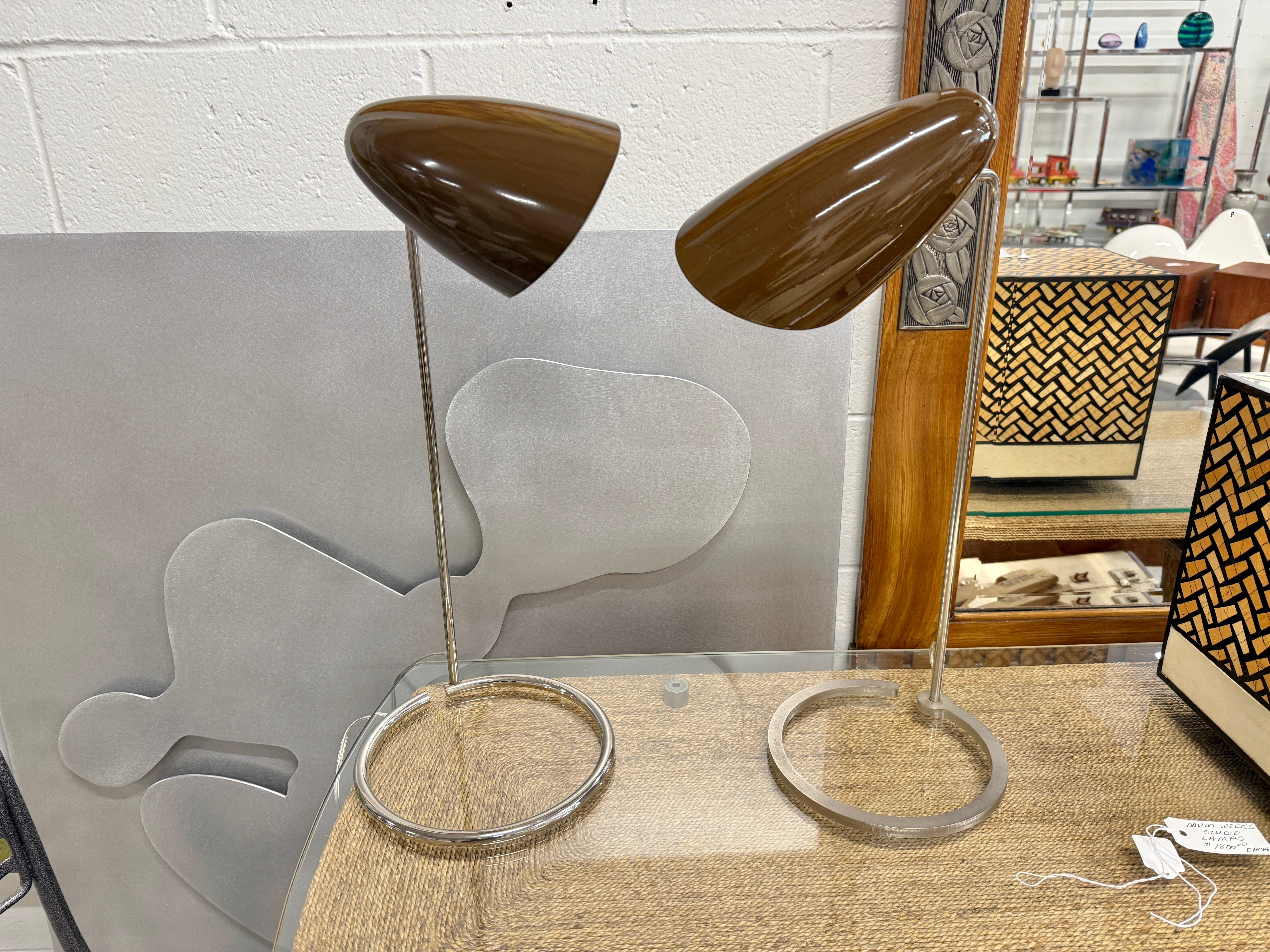 A nice pair of mated table or desk lamps by David Weeks Studio. They feature his iconic bullet lamp head on stands. The lamps are identical except for the bases. While similar in shape they are different. 
The lamps each have a David Weeks Studio