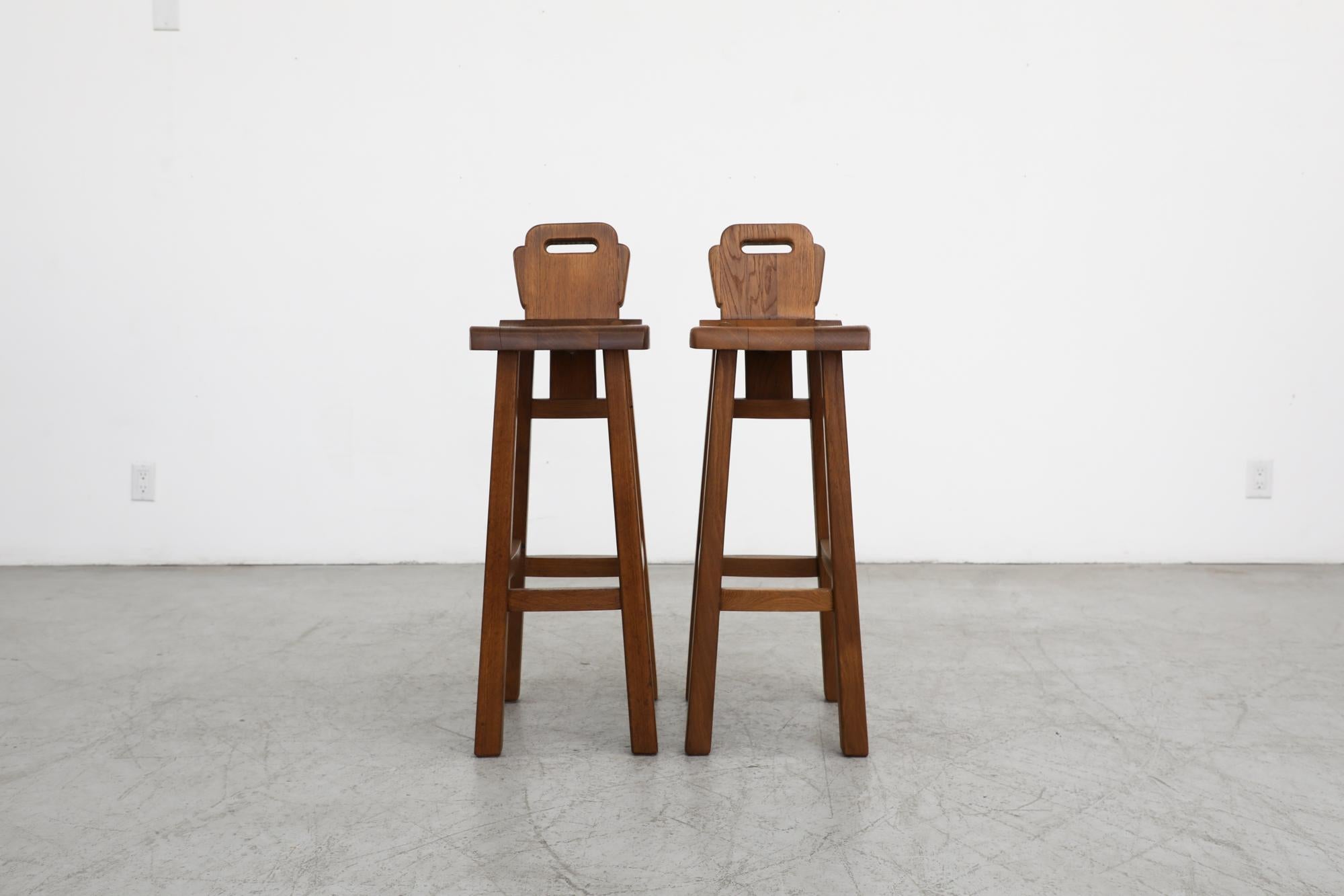Handsome pair of De Puydt attributed Brutalist bars stools. Solid oak frames with beautiful carved details. In original condition with some visible wear and patina, consistent with their age and use. Set price. Similar stools also available in Set