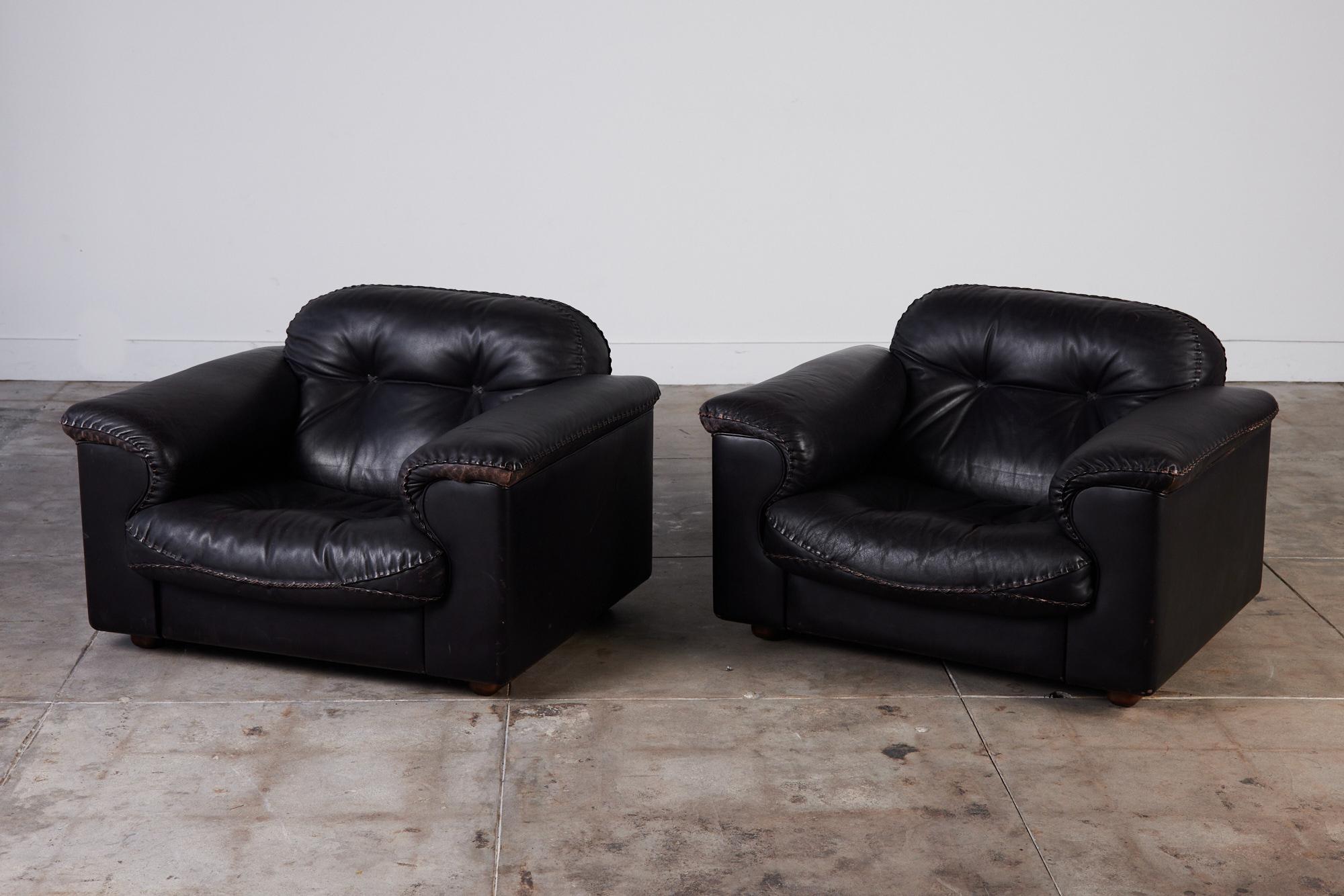 A pair of De Sede leather lounge chairs upholstered in dark espresso leather, c.1970s. These Swiss made chairs feature a reclining mechanism that allows the seats to extend forward while the back rests recline for maximum comfort. The hand stitched
