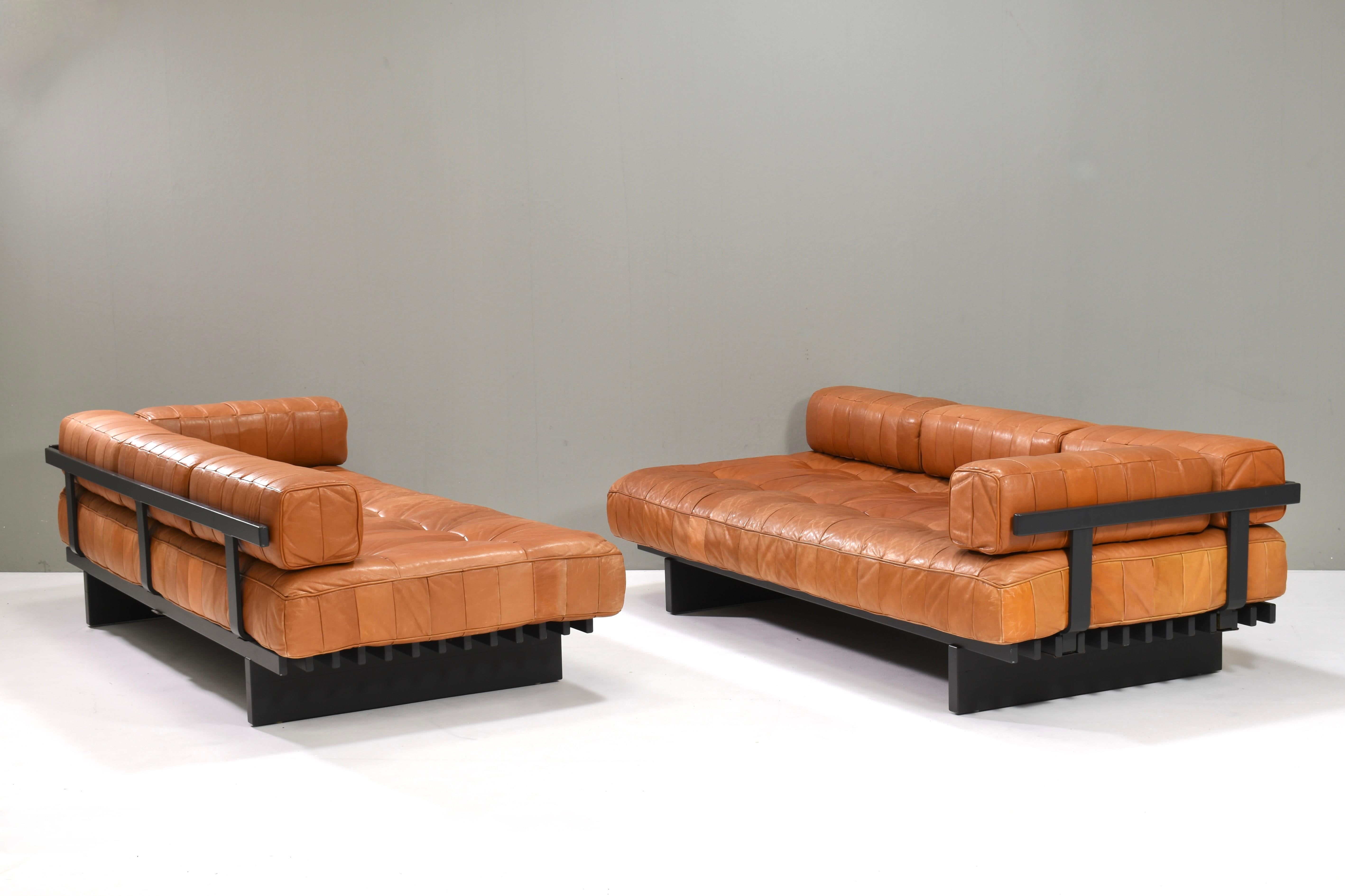 Te presentamos este magnífico sofá cama de retazos DS80 marrón coñac de De Sede. Los soportes de los brazos y el respaldo, de madera lacada, se pueden mover de izquierda a derecha y de atrás hacia delante, para adaptarlos a diferentes