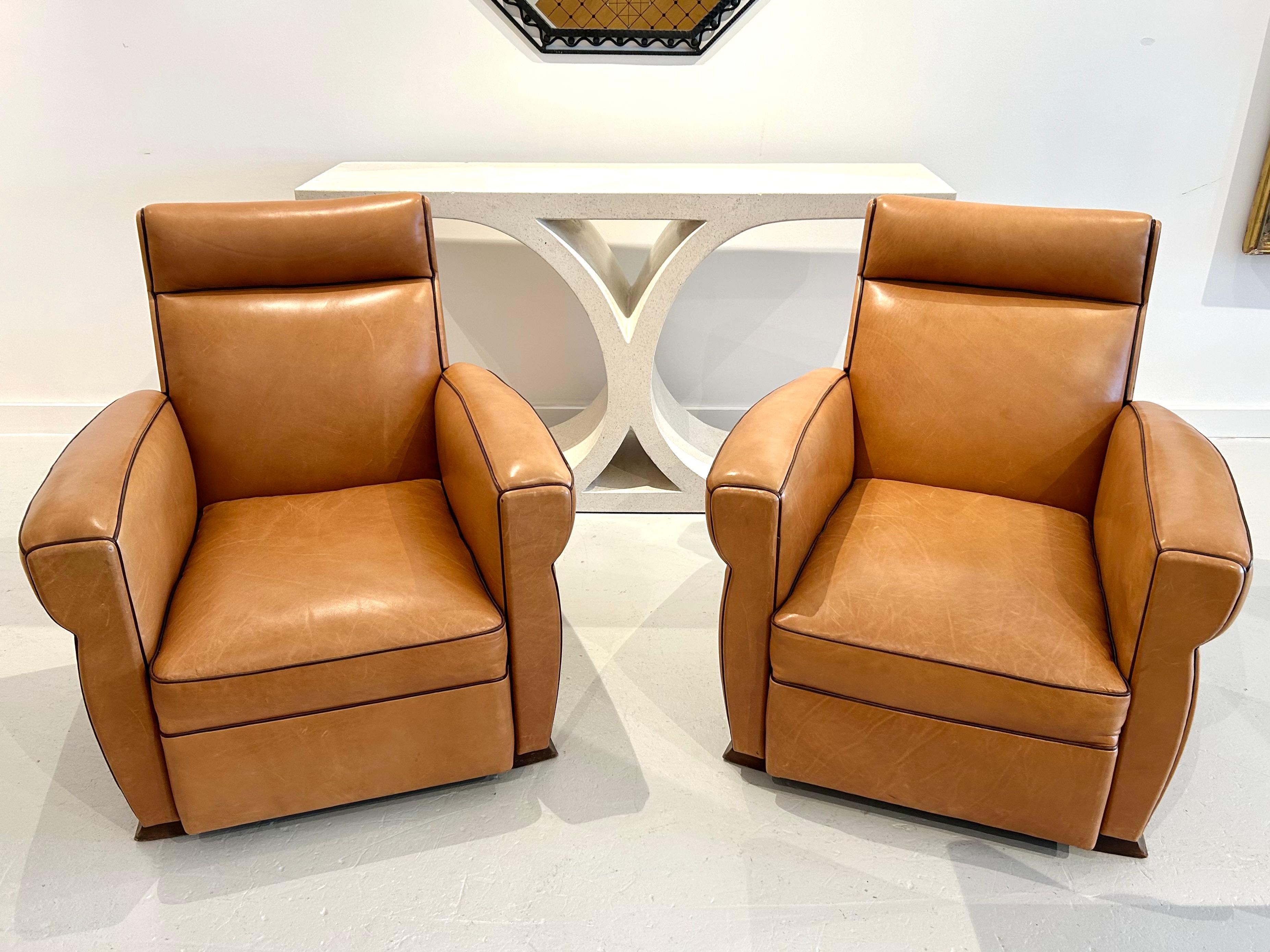 Pareja de sillones club Art Decó muy confortables tapizados en cuero color camel-tan con ribetes de cuero marrón y cabezas de clavos de latón patinado. Se volvieron a tapizar como se muestra aproximadamente hacia 2007. Pies originales de caoba en