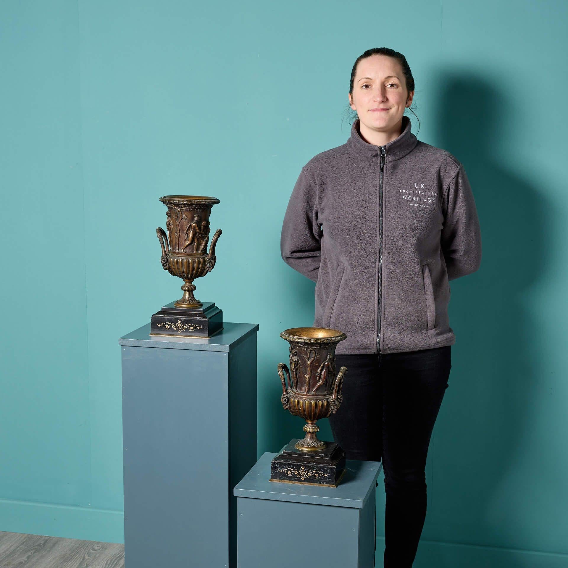 A matching pair of decorative antique bronze Medici style urns, sat upon black marble bases with scroll decoration to the front. Inspired by the design of the monumental 1st century marble Medici Vase, these beautiful antique urns are of campana