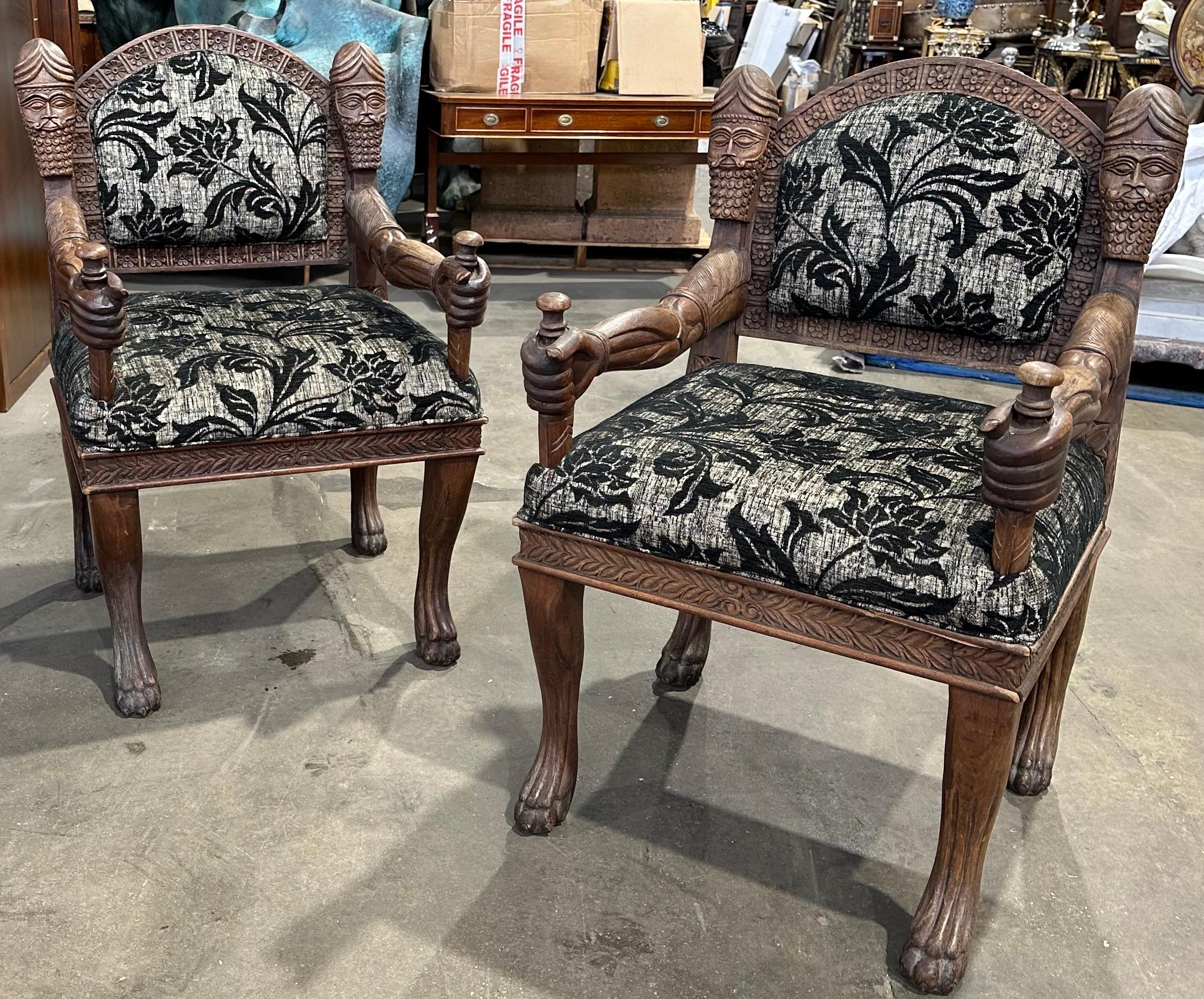 A unusual and decorative pair of hardwood armchairs, upholstered in floral motif fabric. Hand carved with handsome male profiles and curled beards on the chair arms. There is a beautifully carved scene depicting a lion and his prey on the chair