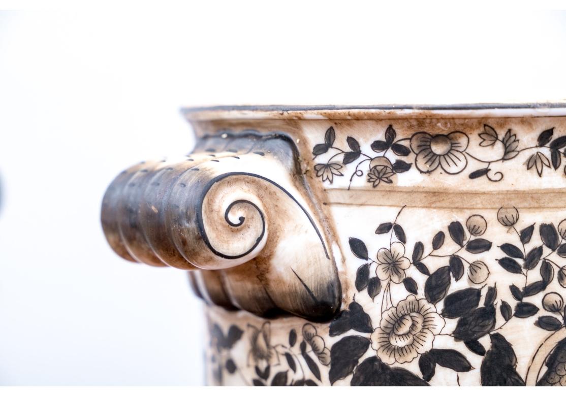 Glazed in brown and white, the cache pots are in the style of 19th century English transferware vessels. There are matching medallions on each side with river landscapes with boats and houses. A pair of opposing dragons fly in the sky. Dense brown