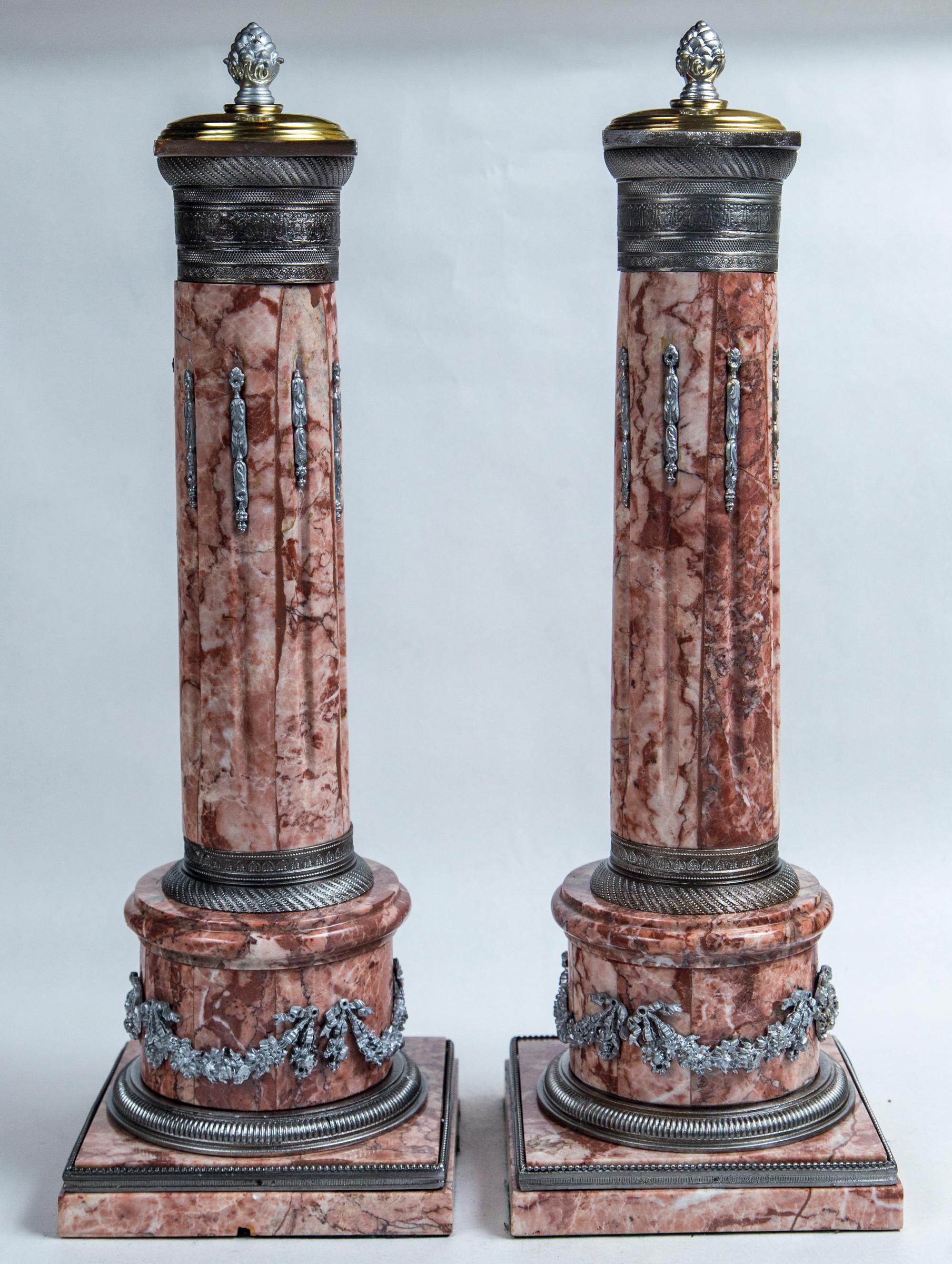 Each column sits atop a square base trimmed in silvered metal. The round column base trimmed with similar decoration and swags. The columns themselves with silvered metal ring and mounts within fluting. The capital and finial also of the same