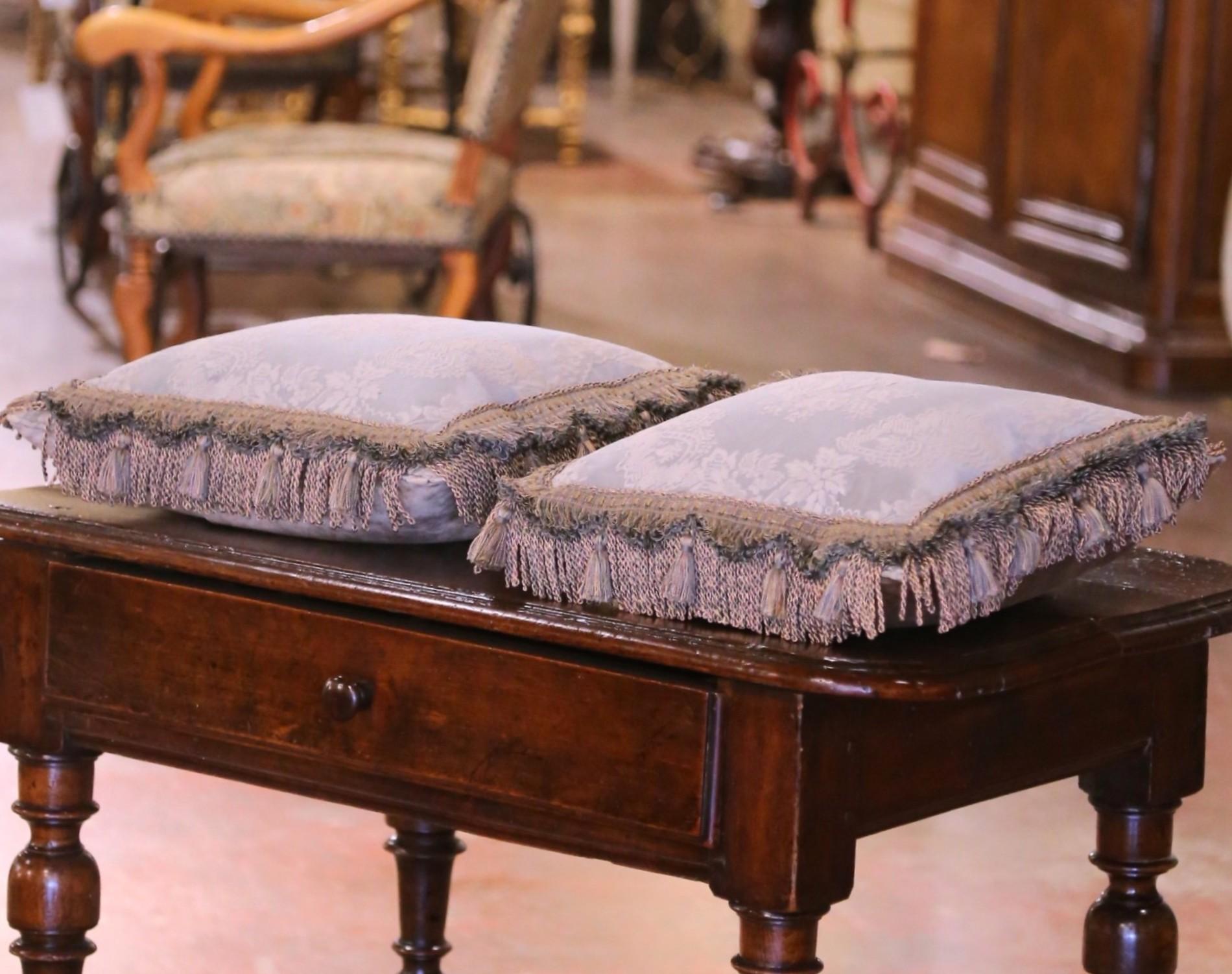 Cette élégante paire de coussins décoratifs vintage met en valeur un savoir-faire exquis et des matériaux raffinés. Fabriqué vers 1980, chaque coussin est de forme carrée et fait de tissu de soie antique dans une teinte céladon argenté pâle, orné de