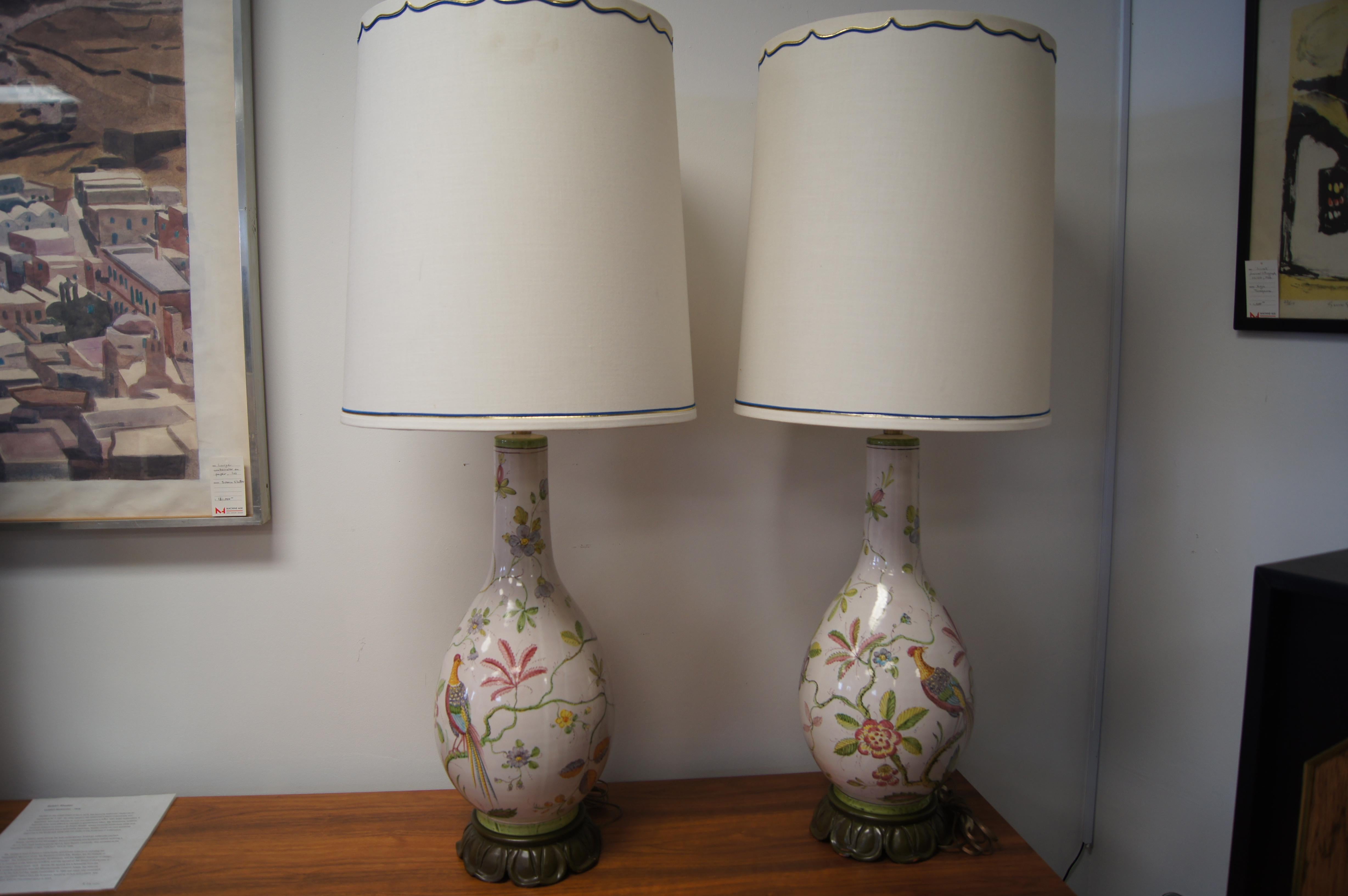 This pair of table lamps by Marbro depicts pheasants among flora in a lovely mélange of reds, blues, greens, lavenders, yellows on a cream ground. The long tapering porcelain body sits on a carved and patinated wooden base.

Listed as model no.