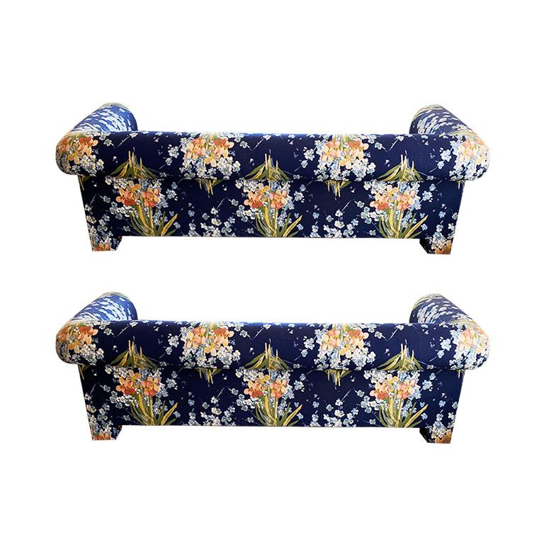 A lovely pair of blue floral sofas by Henredon. This pair features rolled arms and very deep bench seats. Perfect for spooning. Peach and green floral bouquets decorate the piece on a deep blue background. The four legs are square cornered. This