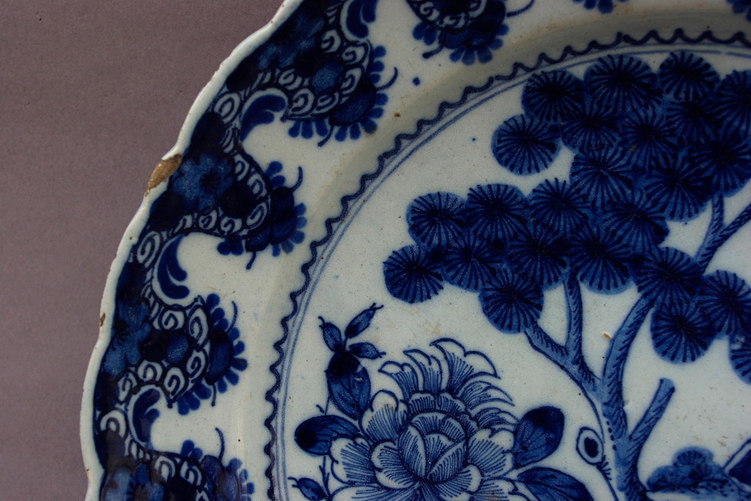 Pair of blue and white delftware plates imitating Chinese porcelains. Blue decoration on a white background underlined with a trek, representing a tree surrounded by flowers in vases. Lambrequins and stylized plants friezes inside, typical of this