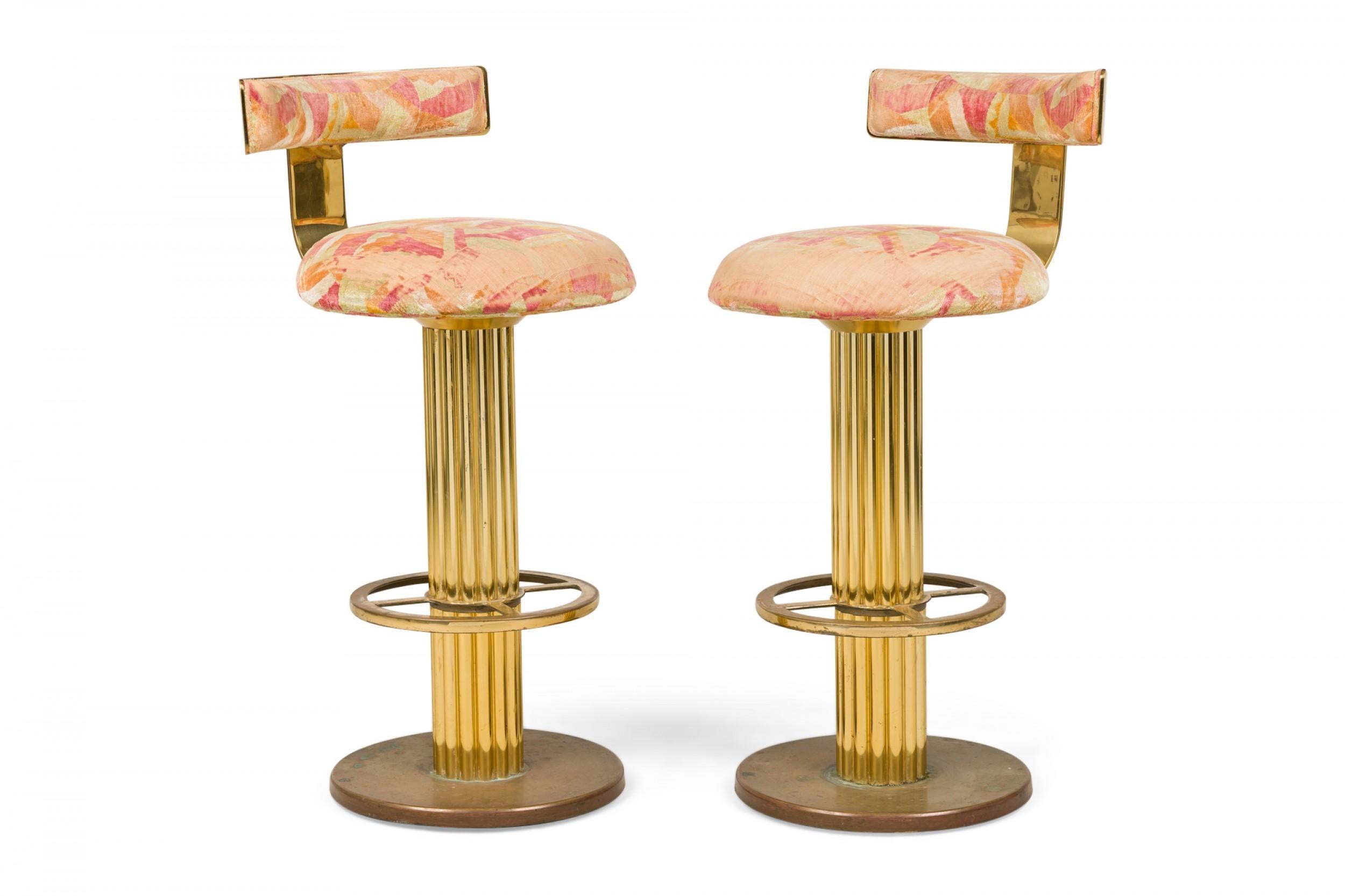 PAIR of Mid-Century American brass swivel bar stools upholstered in a peach palette geometric chenille with low curved backrests, supported by thick fluted column bases plus pierced foot rings, resting on circular bases. (DESIGNS FOR LEISURE)