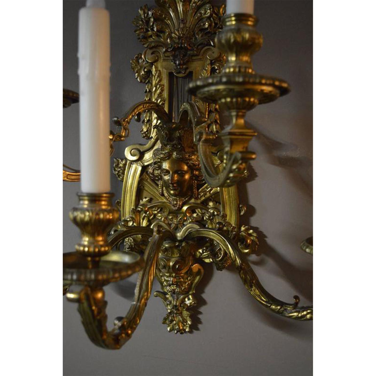 Pair of detailed bronze sconces. There is a female face at the centre of the sconce and a male face at the bottom.