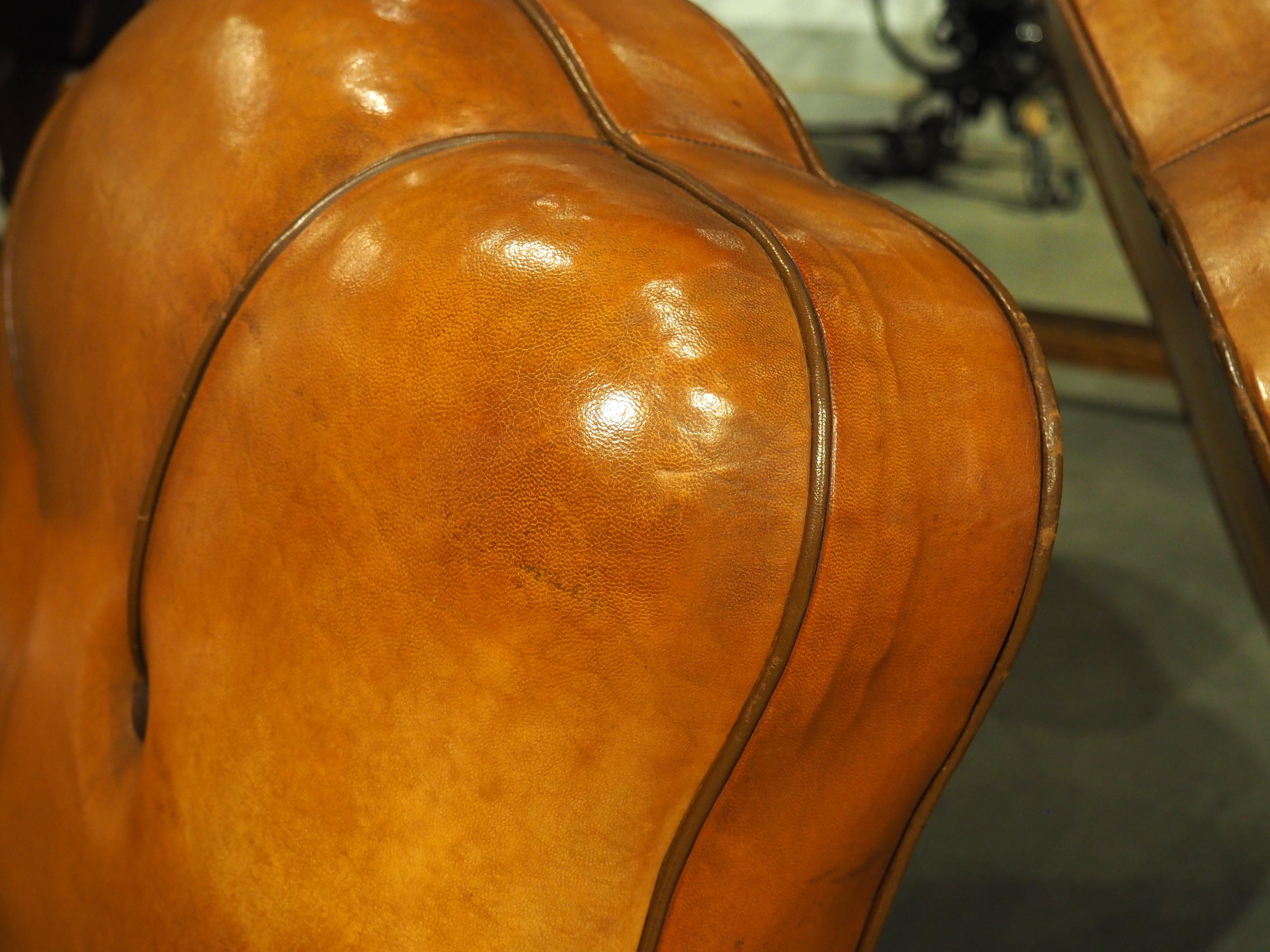 The soft and supple form of this pair of diminutive French leather club chairs is quite inviting. Dating to the (circa) 1930s, the slightly arched seatbacks have two piped tufts that terminate under a button about halfway up the back. The seats are