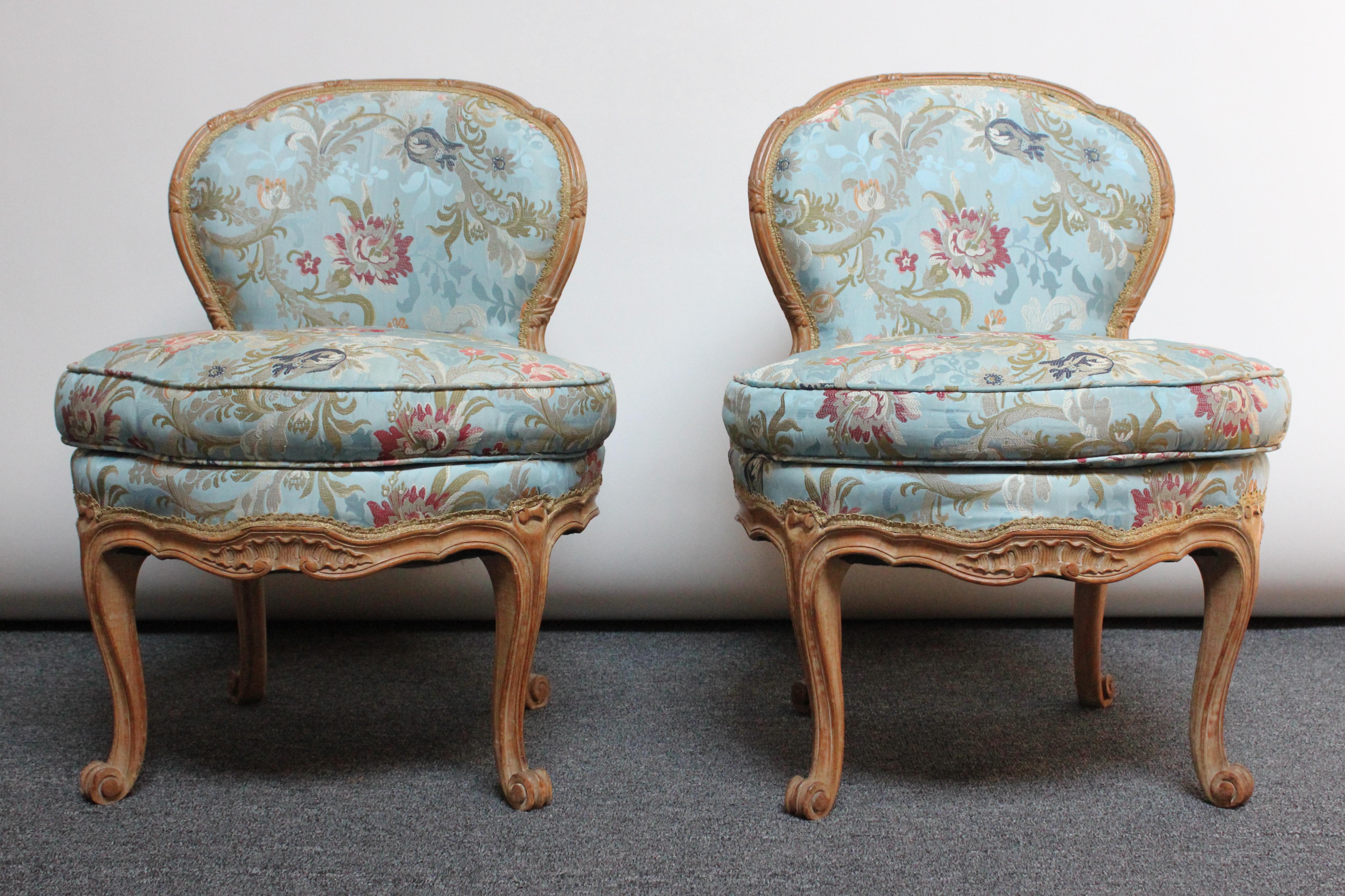 Petite Louis XV-style boudoir / vanity chairs with carved oak frames and scroll cabriole legs (ca. 1900, France). Features carved acanthus and leaf motif throughout. 
Floral silk upholstery is a later addition (likely 1930s-1940s) and shows light