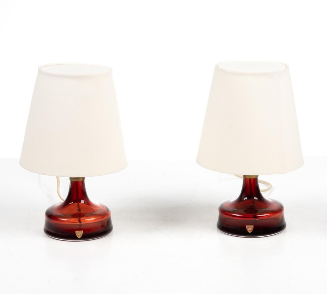 This adorable pair of table lamps by Carl Fagerlund for Orrefors features jewel-like bottle bases in ruby cased glass, with patinated brass socket mounts and cream linen shades. Both are signed with hand-etched 
