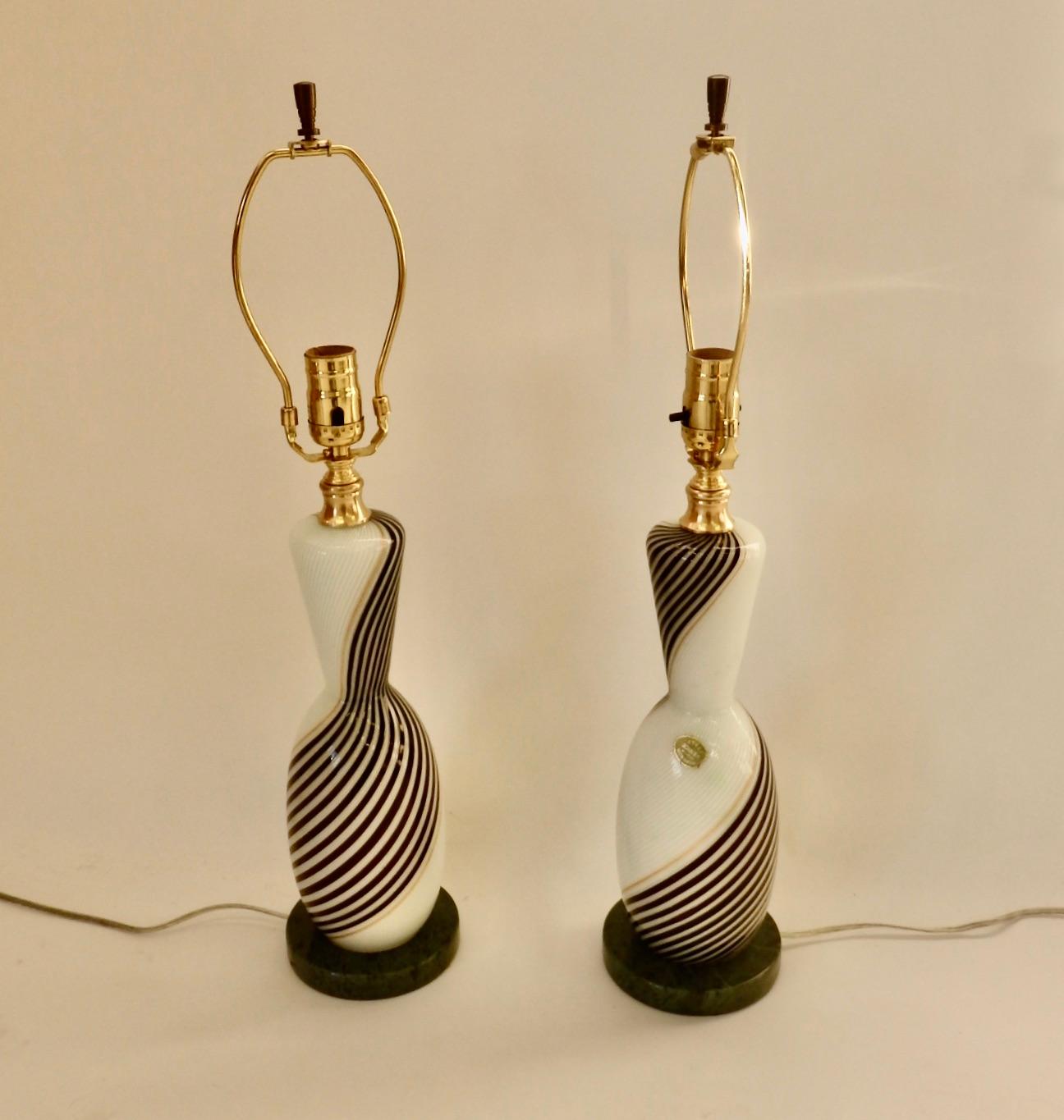 Pair of Dino Martens table lamps. Original label reads Murano glass Venice Italy. Black and white swirl with gold detail. Freshly wired on green marble bases. Original finials included.