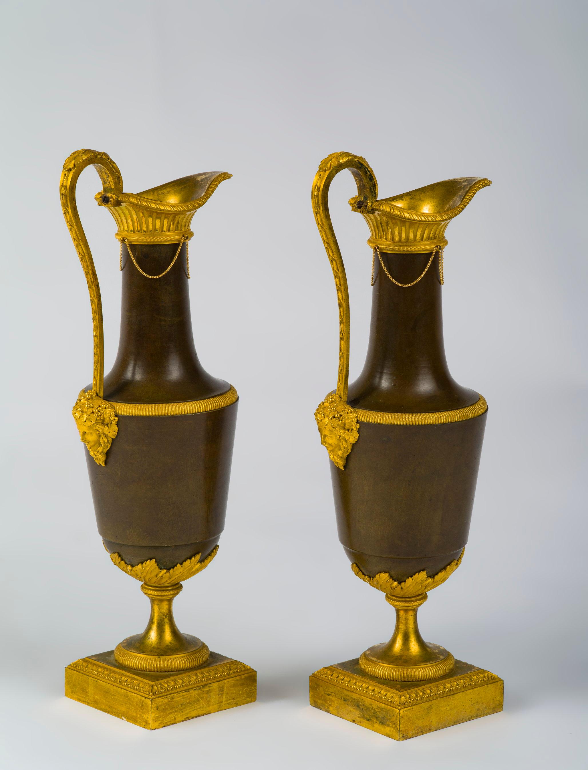 In the neoclassical taste, the open reeded spouts above ovoid bodies with leaf-clasped socles on square bases, the handles terminating in a female mask.

This pair of ewers is a rare early example of a model which became more popular under the