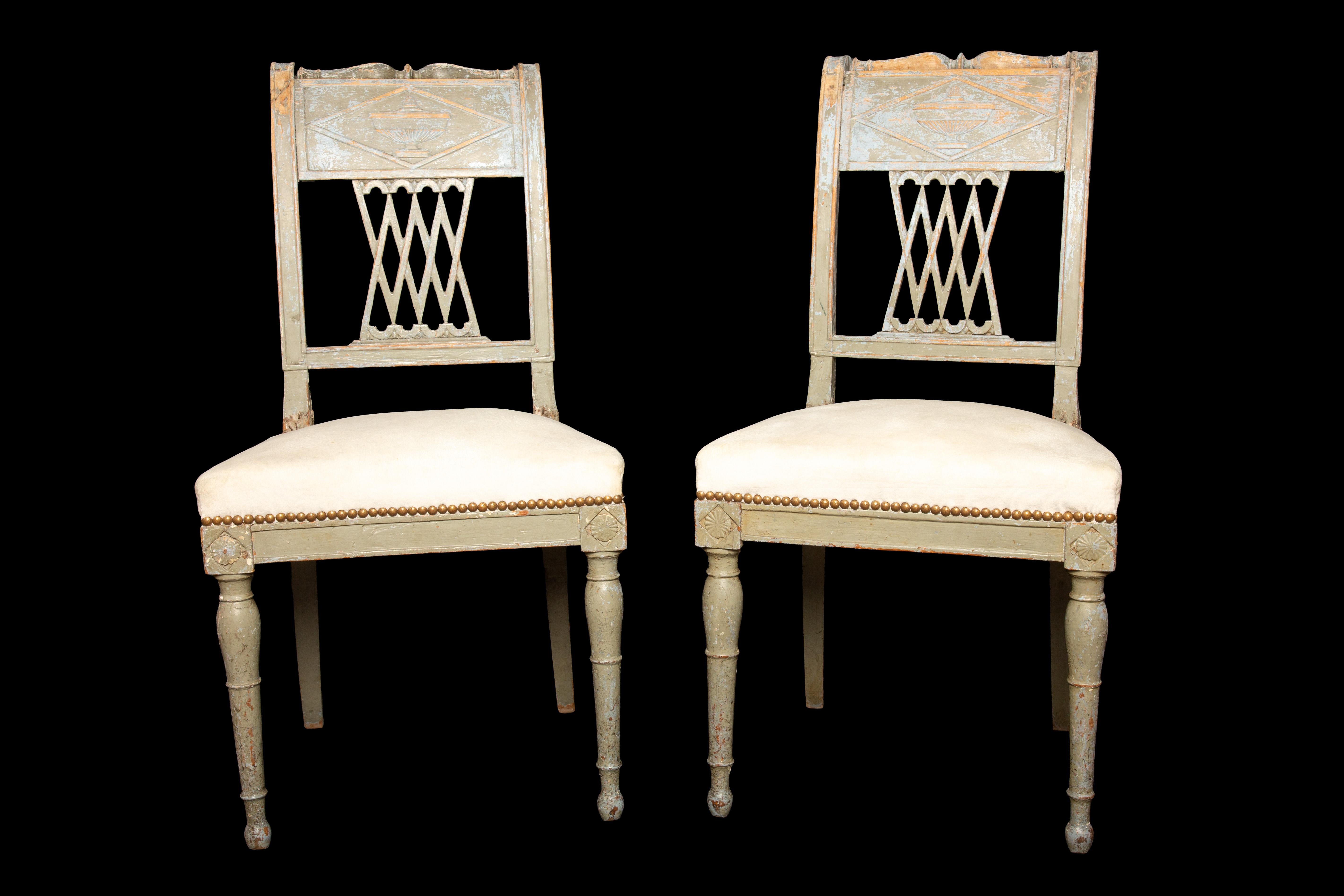 This exquisite pair of painted beechwood chairs showcases the elegance and artistry of the Directoire period (1795-1799). The chairs feature a captivating openwork back adorned with intricate crosses and delicate vase motifs, displaying the skilled