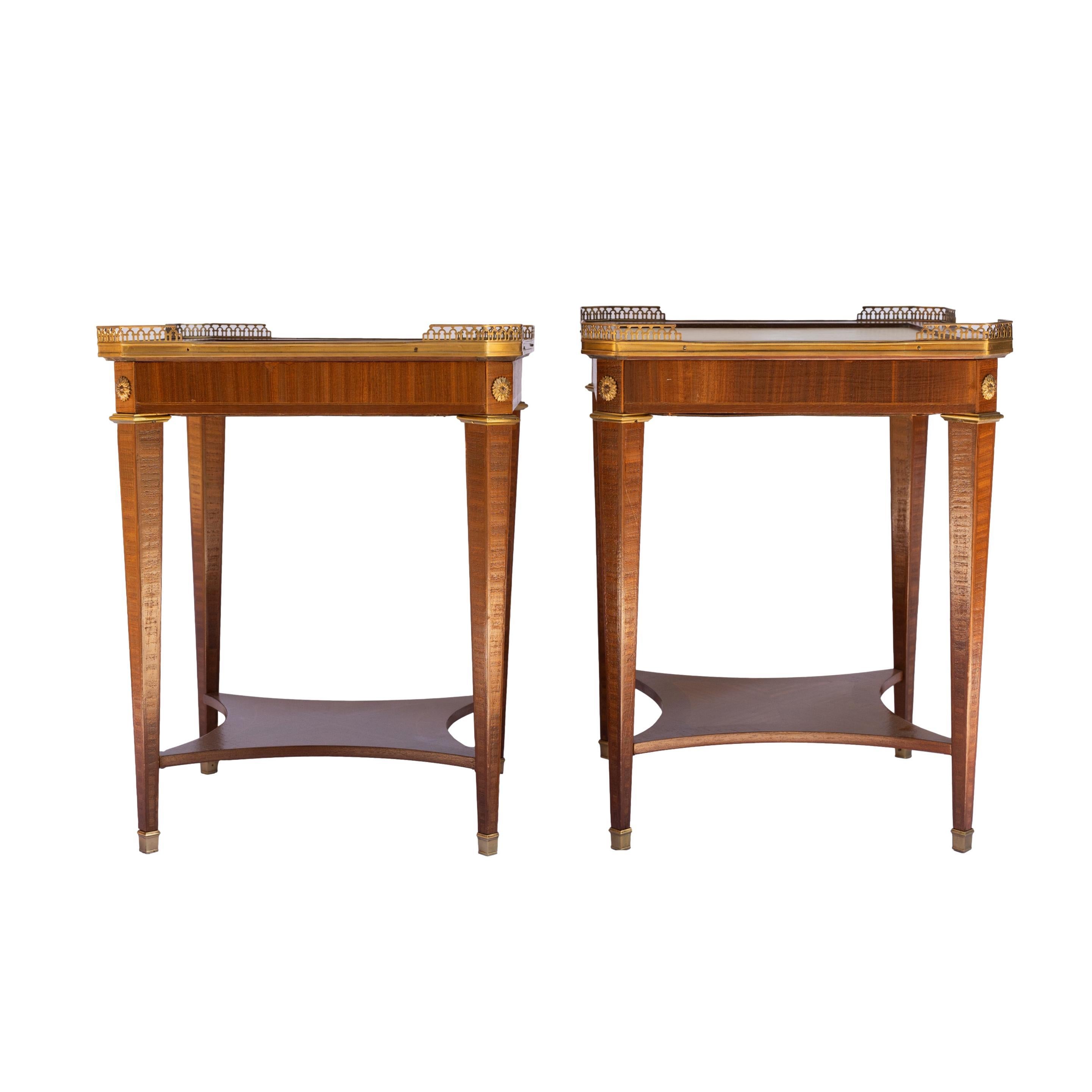 A Pair of Mahogany Directoire-stye side tables with bronze ormolu mounts and gallery, with tooled leather top, and shaped shelf below, on tapered legs terminating in bronze sabots, French, ca. 1920.  