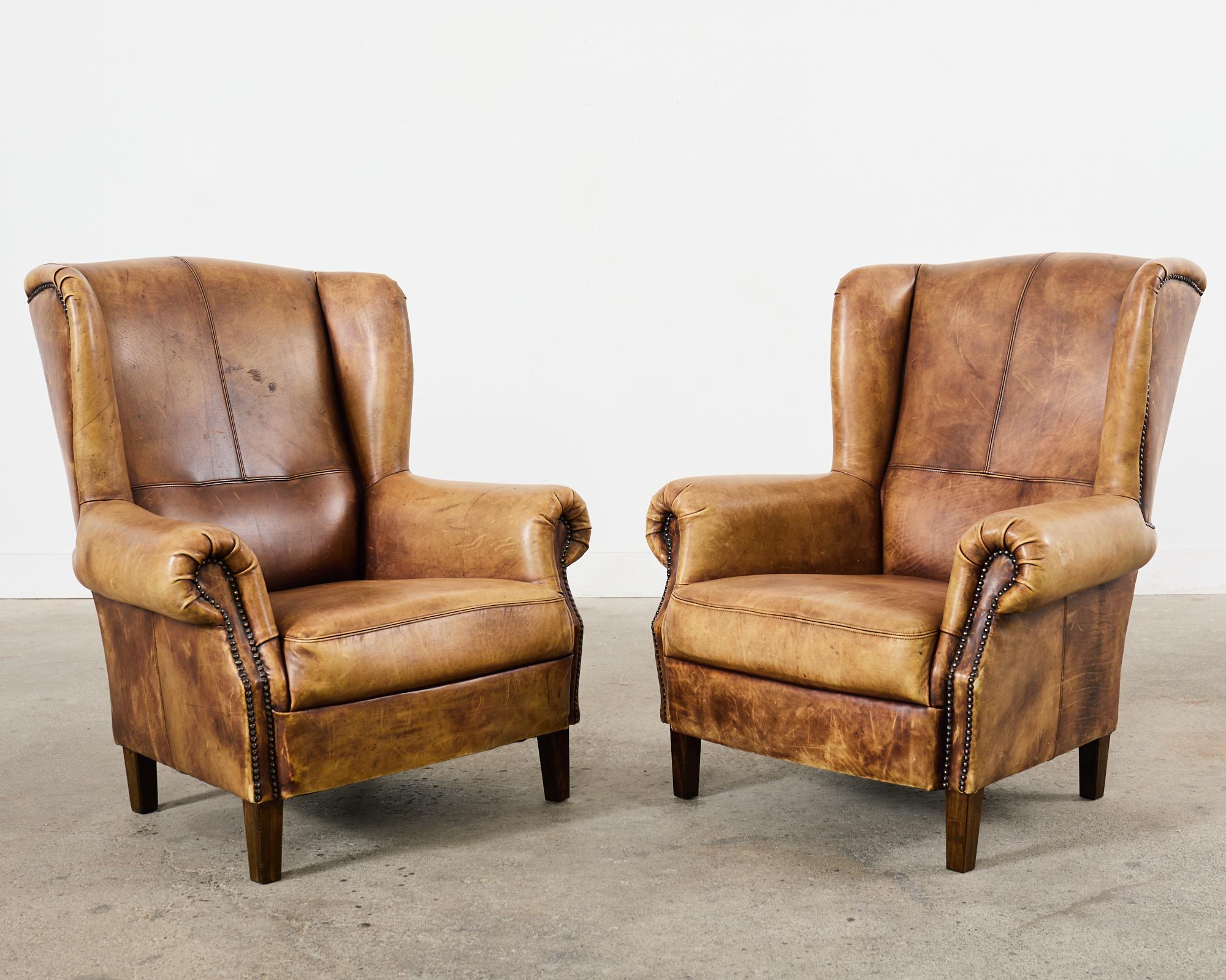 Patinated Pair of Distressed Cigar Leather Wingback Chairs with Ottomans