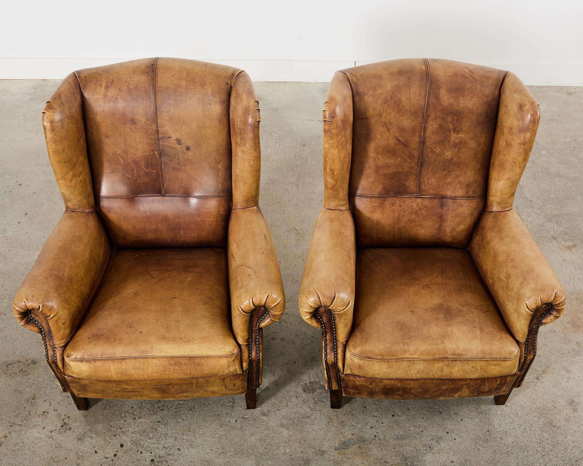 Brass Pair of Distressed Cigar Leather Wingback Chairs with Ottomans
