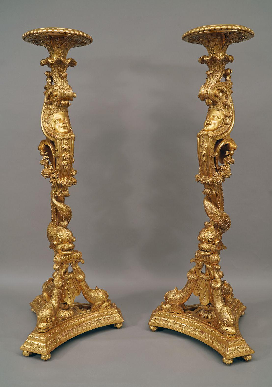 Exceptional pair of Regence style carved and giltwood torcheres holders. The console shaft around which a dolphin is wrapped is richly decorated with leafy scrolls, shells, floral falls and a woman mask. It supports a circular top with palmette and
