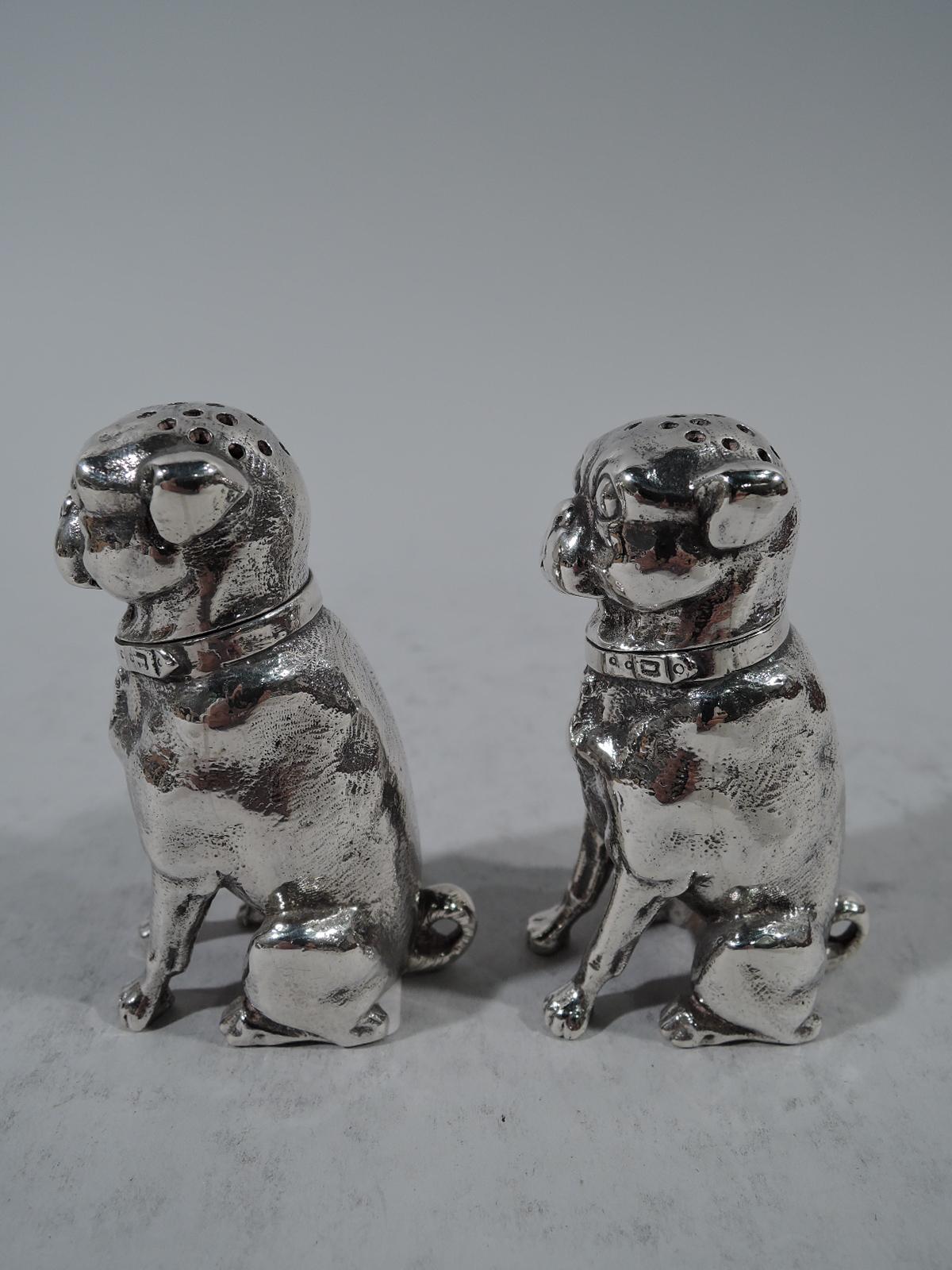 Pair of sterling silver dog-form salt and pepper shakers. Made by Dominick & Haff in New York in 1879. Each: cast figure of stocky seated pup with stiff forelegs and curlicue tail. Flat face with exophthalmic eyes and short snout. Head pierced and