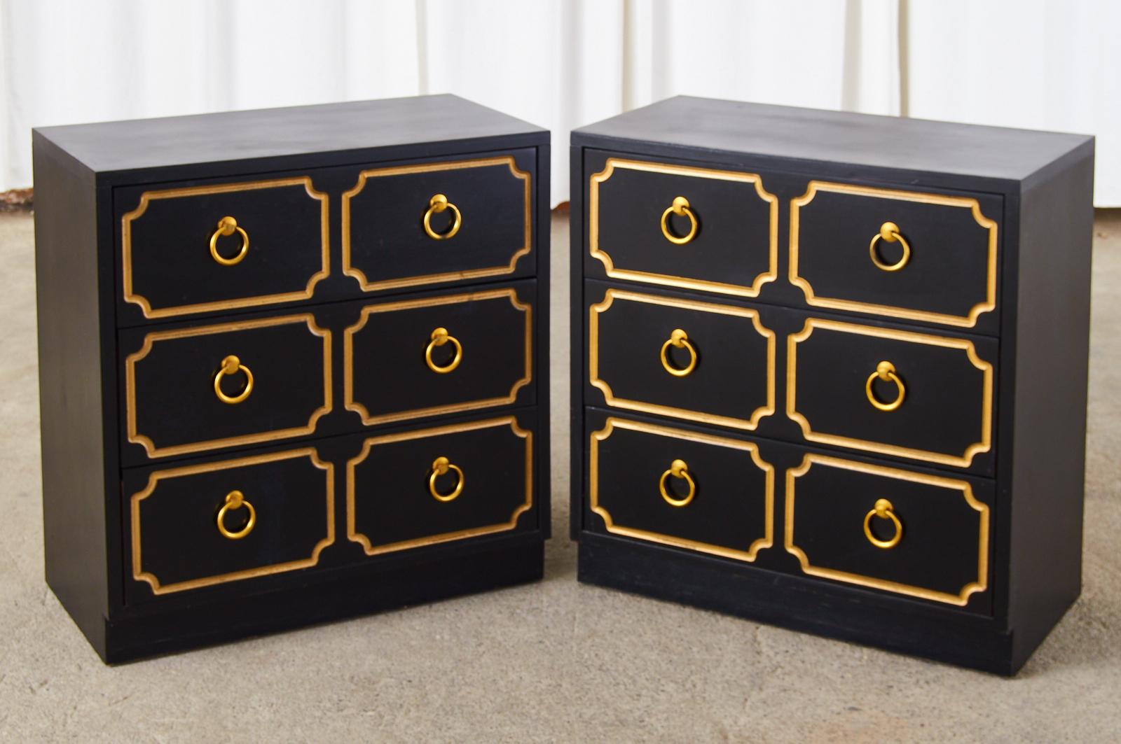 Matching pair of black and gold chest of drawers or commode dressers in the iconic style and manner of Dorothy Draper's Espana model. Hollywood Regency chests fronted by three drawers having pairs of brass ring pulls. The drawer fronts are decorated
