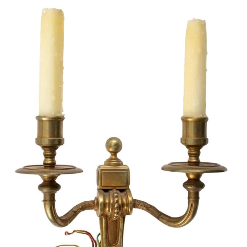A vintage pair of double arm gilt bronze neoclassical wall sconces. The center stem is tapered with a ball finial at top and bottom and a textured finish to the center. The arms are each curved with acanthus leaf detail and meet in a half sphere