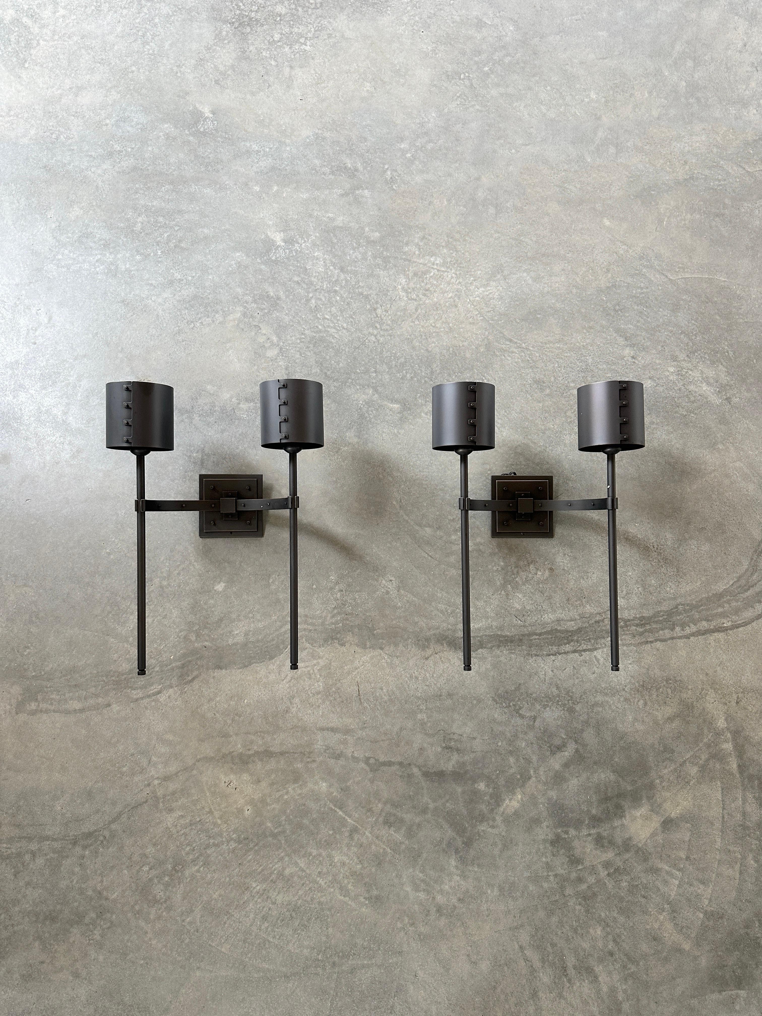 These Aureole sconces feature a sleek and minimalist design, with a rectangular backplate and two cylindrical shades that emit a soft and warm light. Heavy bronze handcrafted into a simple and clean design with subtle cast bronze detailing. Created