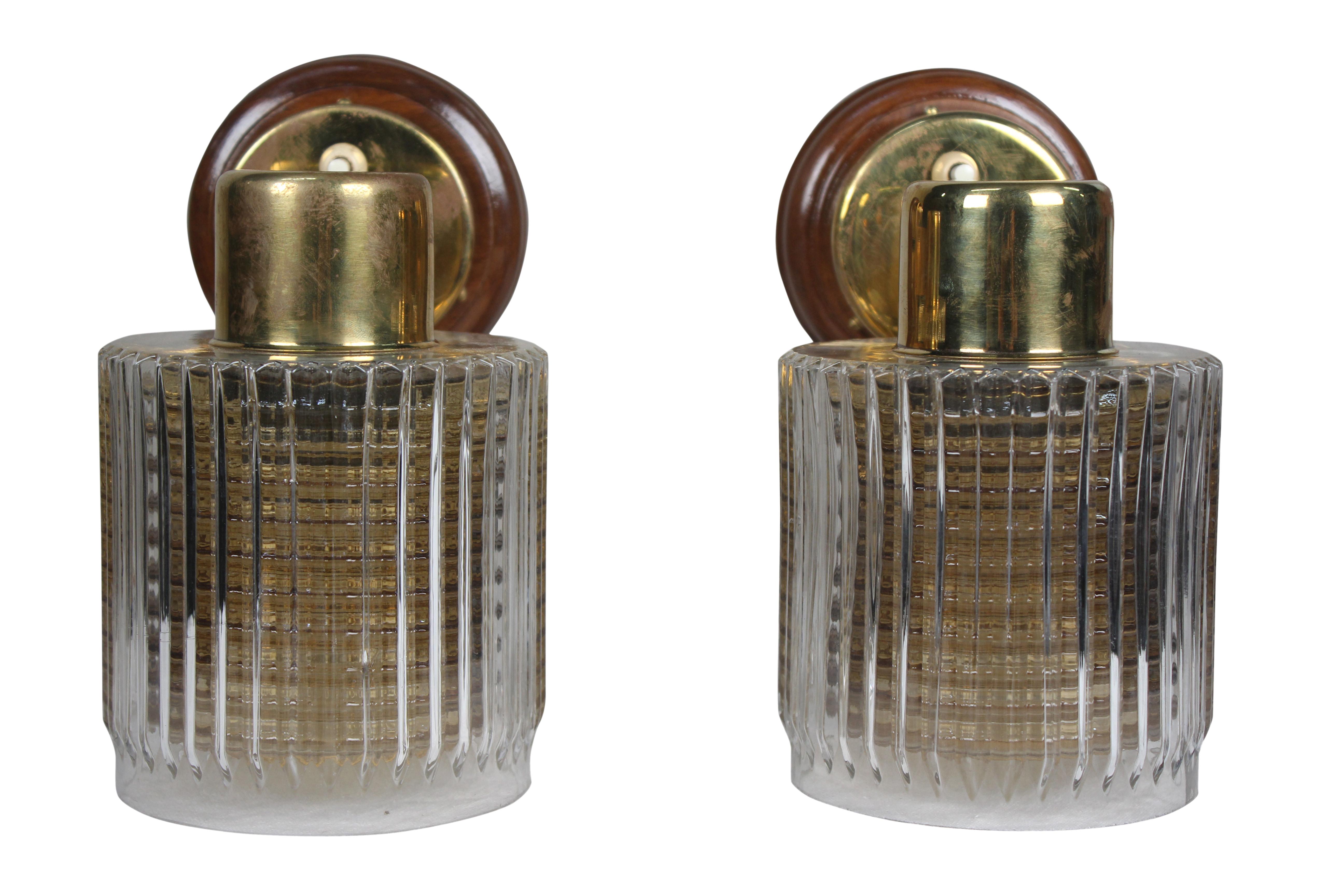 A pair of brass wall sconces with teak back plate with double glass shades. The interior shade is an amber color and the exterior shade is a textured clear glass, mid-20th century. Rewired for American use and takes a standard base light bulb.
