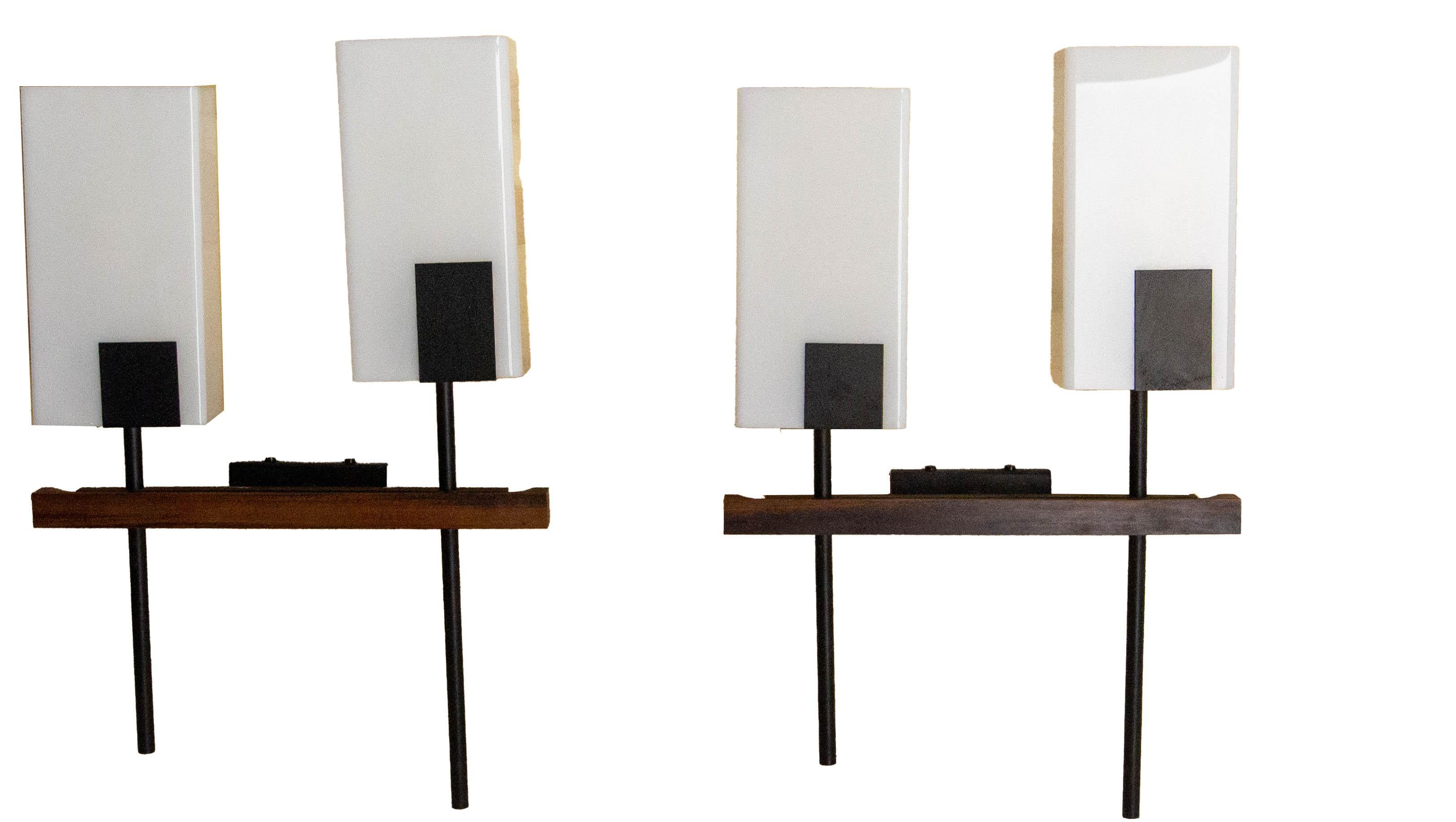Pair of wall lights with a geometric design typical of the 1960s, combining a black metal structure, a wooden base, and a rectangular opal glass diffuser. 
The clean lines and contrasting materials reflect the influence of the modernist design of