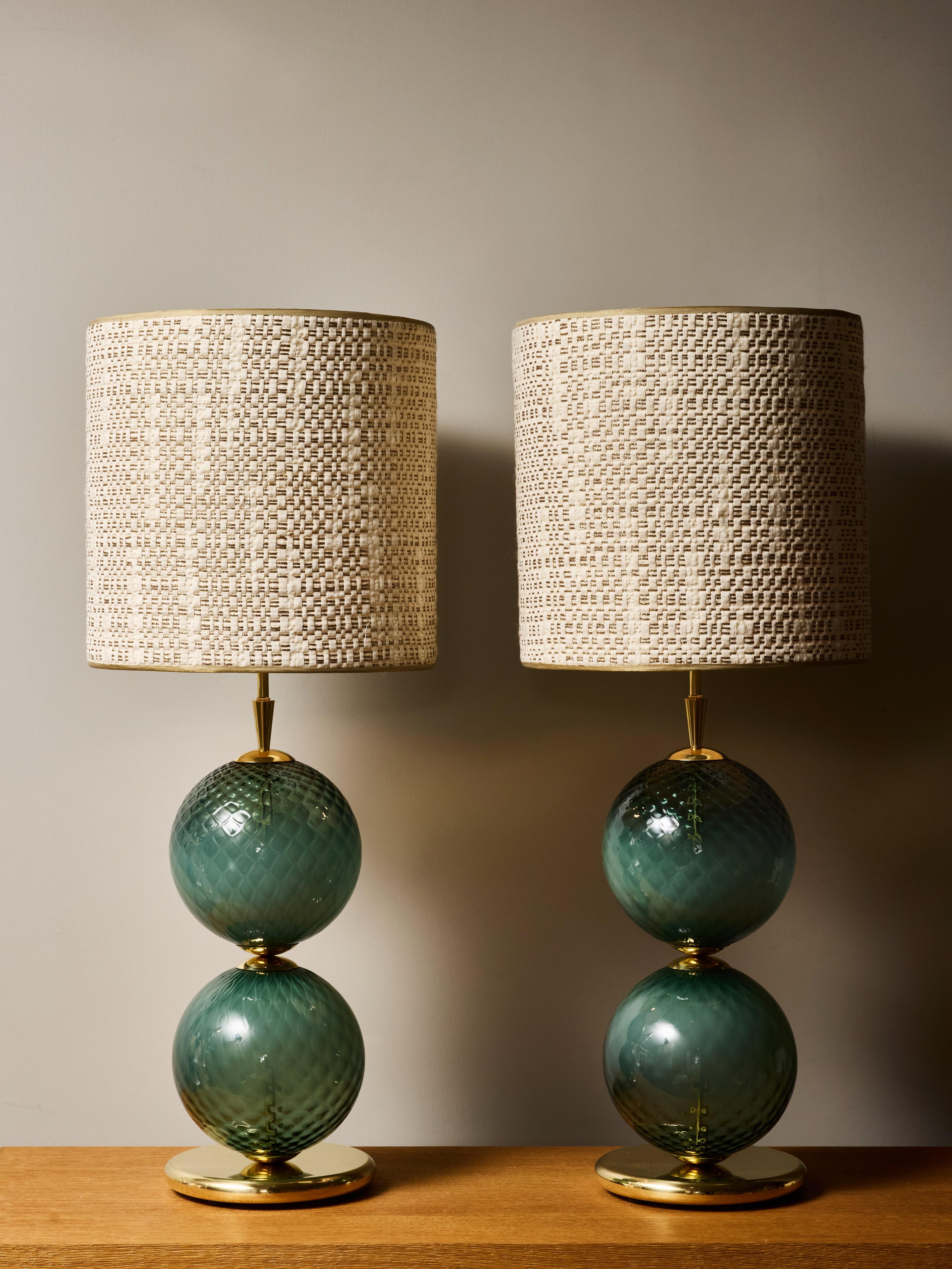 Un llamativo par de lámparas de sobremesa de vidrio artístico contemporáneo, cada una compuesta por dos esferas sopladas a mano en un rico tono verde ahumado con una intrincada superficie texturizada en forma de diamante. El vidrio exhibe una