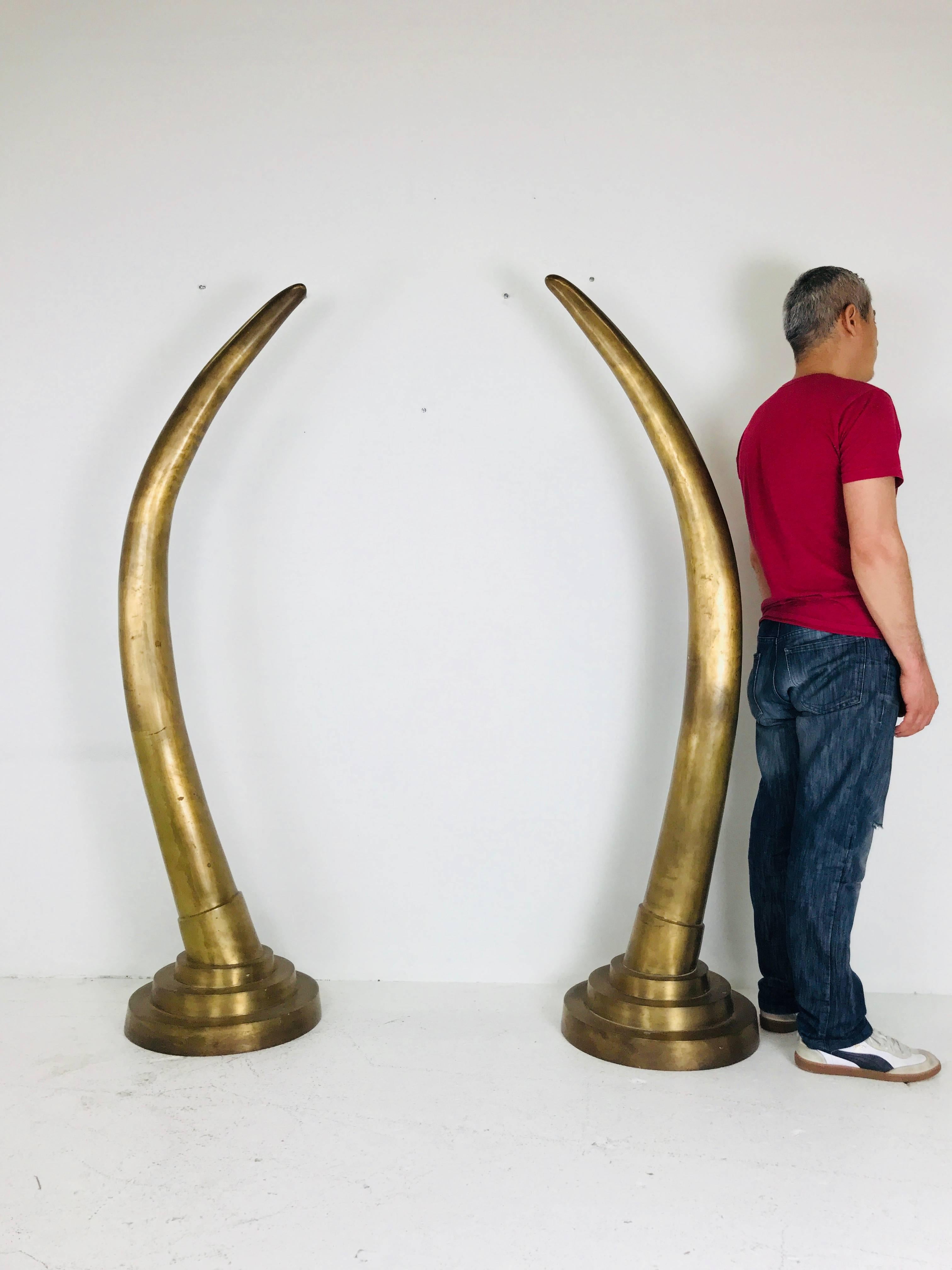 Pair of dramatic brass tusk statues. These brass tusk statues can drama to any room. The brass has an aged patina and has some minor dents in finish.

Dimensions: 16