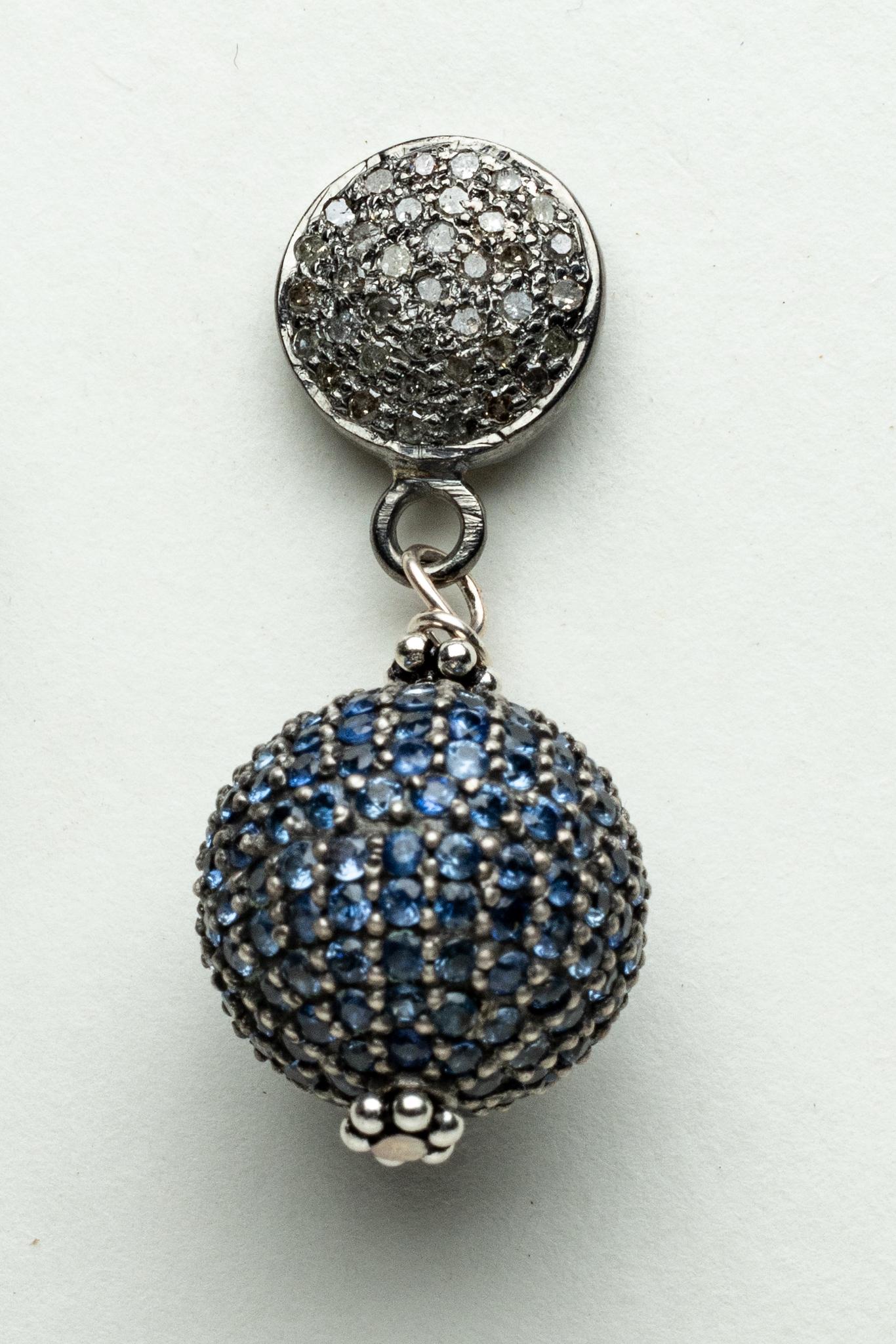 Paire de boucles d'oreilles boule avec des saphirs bleus ronds et facettés dans un serti pave couvrant la totalité de la boule.  La monture est composée de diamants ronds, de taille brillante, également en serti pave.  Les diamants totalisent 0,65
