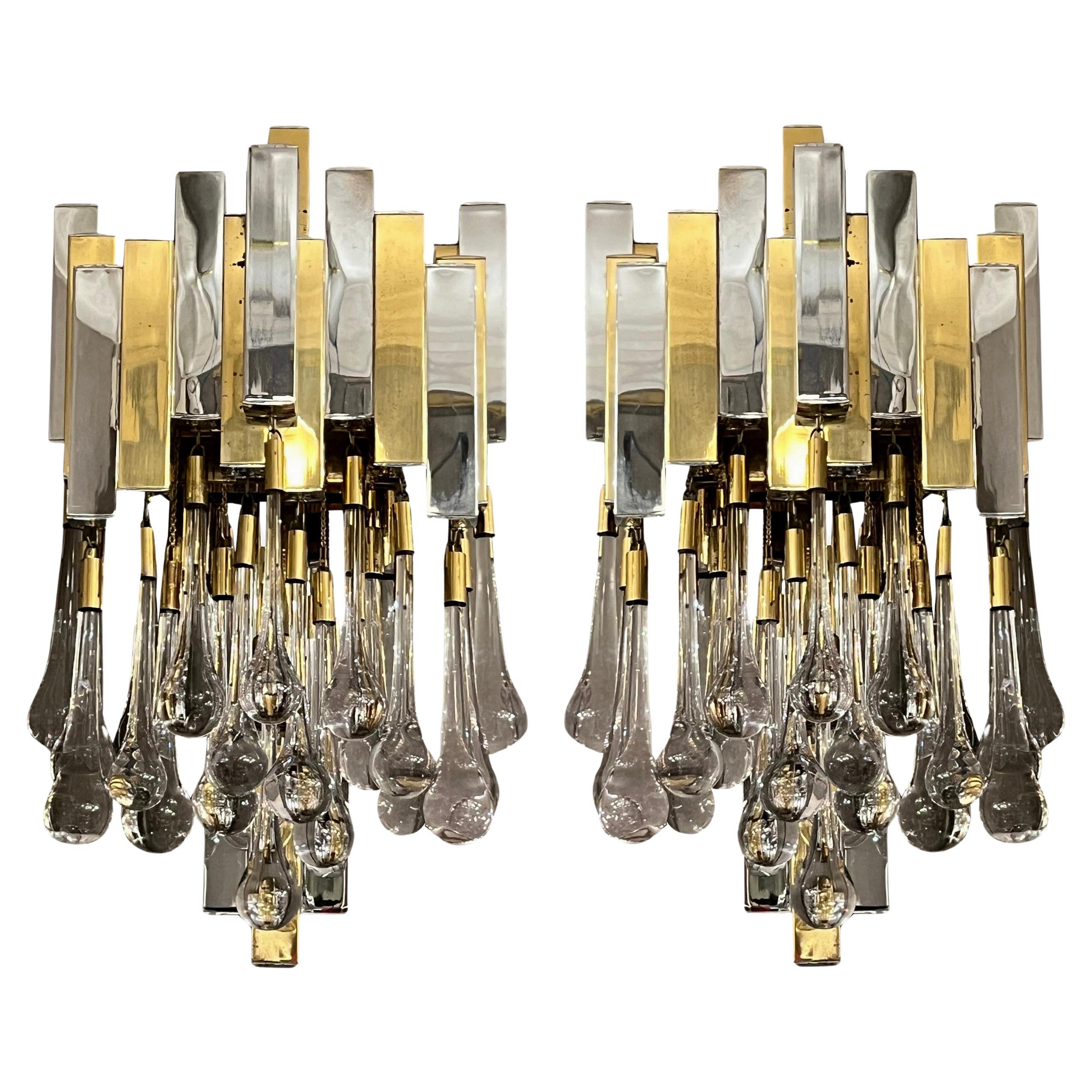 Pair of important « drop » sconces by Lumica , Barcelona, circa 1970.
A structure of square brass and chrome-plated brass tubes, closed by chrome-plated cabochons, supports twenty solid glass drops concealing three light bulbs.