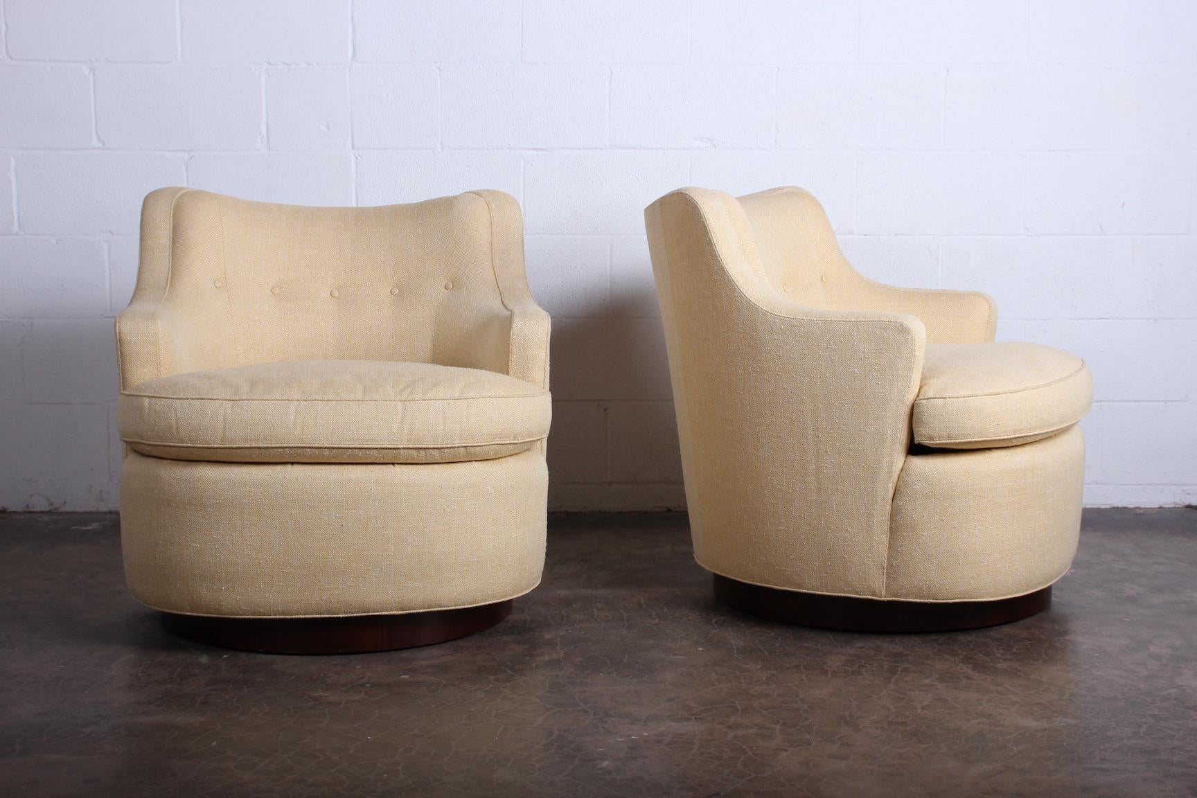 A pair of large scale swivel chairs on mahogany bases designed by Edward Wormley for Dunbar. Fully restored with down cushions and upholstered in Cowtan and Tout cotton in a neutral straw yellow weave.