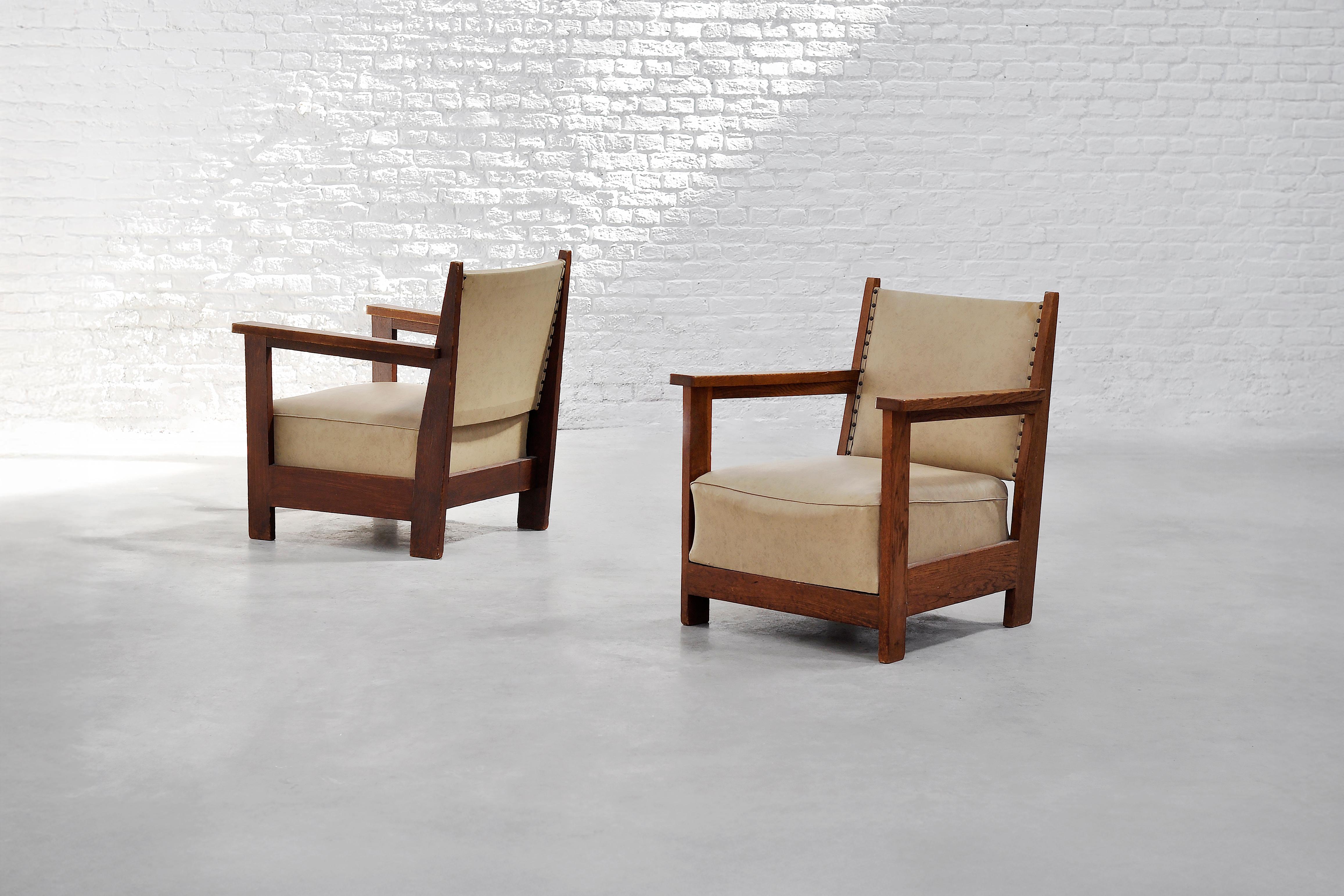 A pair of lounge chairs rooted in the Dutch Art Deco tradition of the 1930s, reflecting a harmonious balance between robust construction and minimalist design. These chairs are crafted from solid oak, with clean vertical lines, square arms, and a