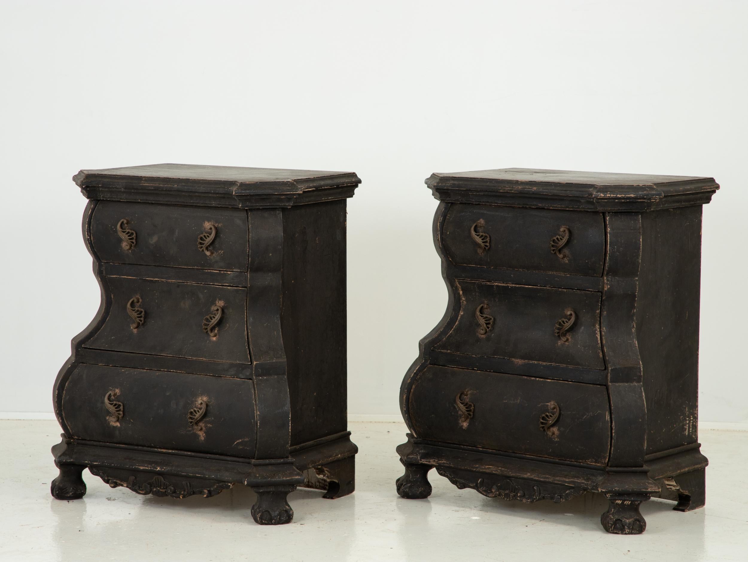Stunning antique late 19th century pair of Dutch bombes or dressers made in the Netherlands in the late 19th century. Sinuous serpentine silhouette painted in a rich black. Carved scroll at the base is complemented by naive carved paw feet. Dressers