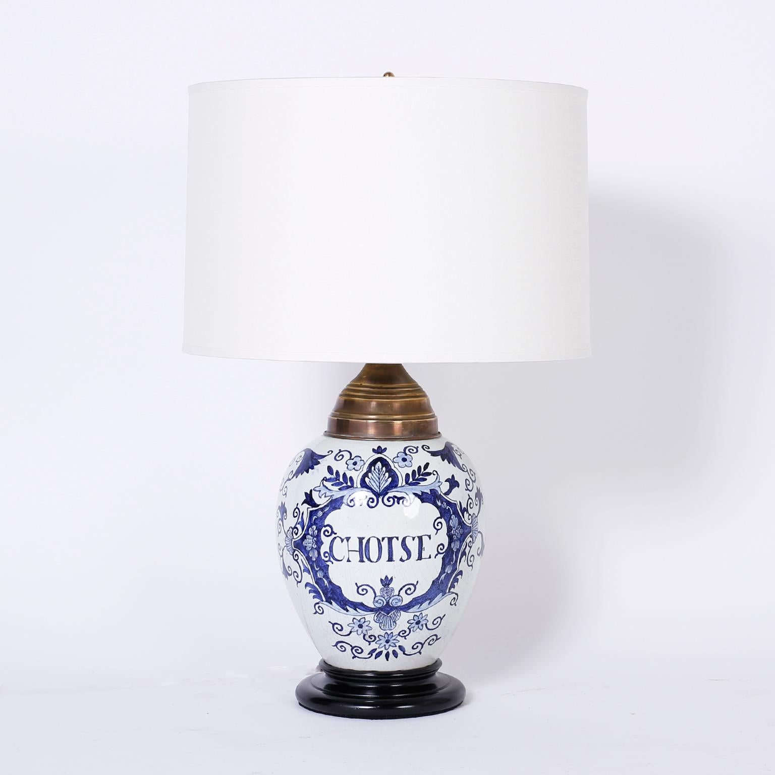 Charming pair of Dutch colonial style tobacco jars converted into table lamps. They are hand decorated with blue flowers and words that translate to miscellaneous and tobacco. Presented on turned wood ebonized bases.